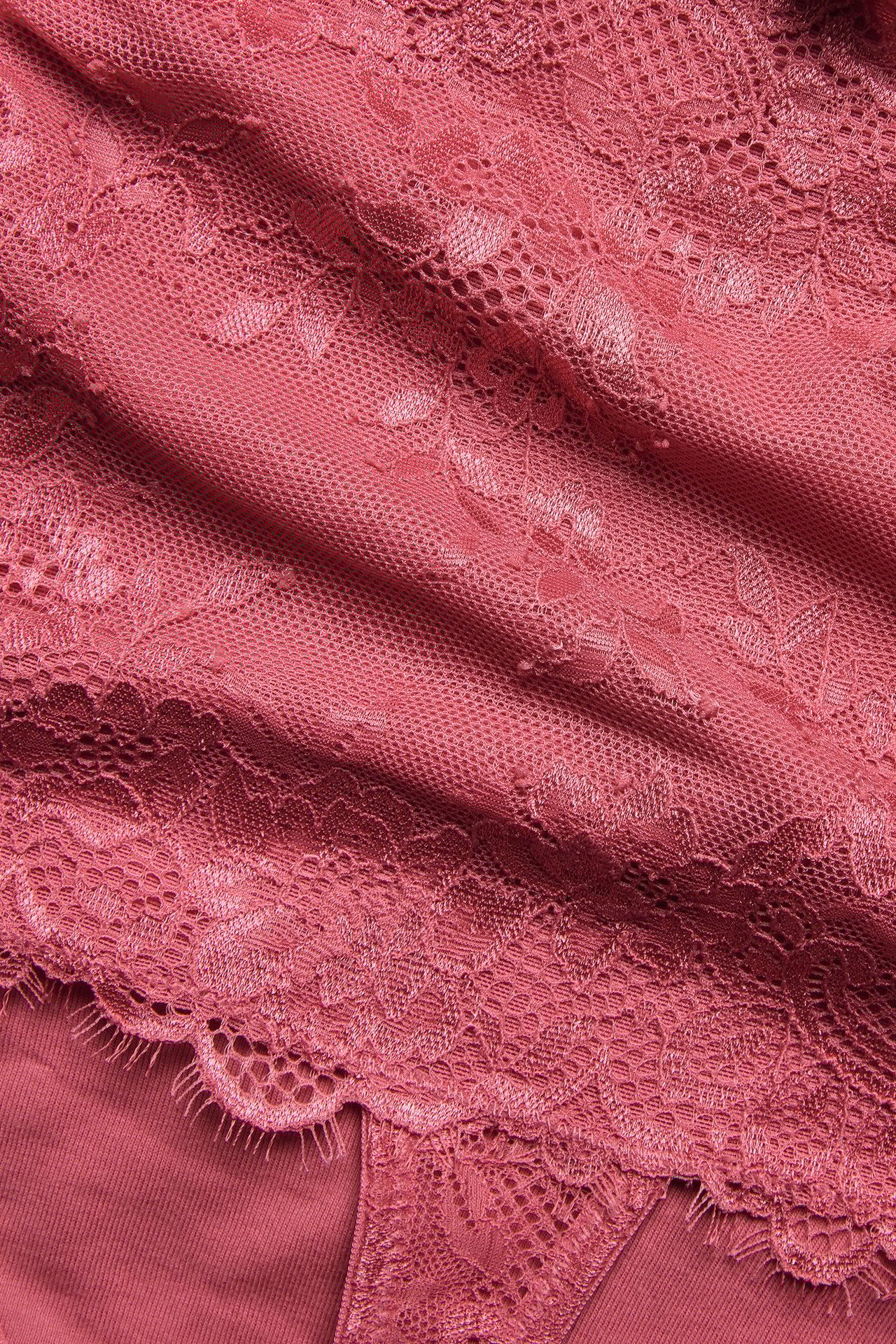 Zbliżenie koralowych koronkowych stringów z wysokim stanem i kwiatowym wzorem.