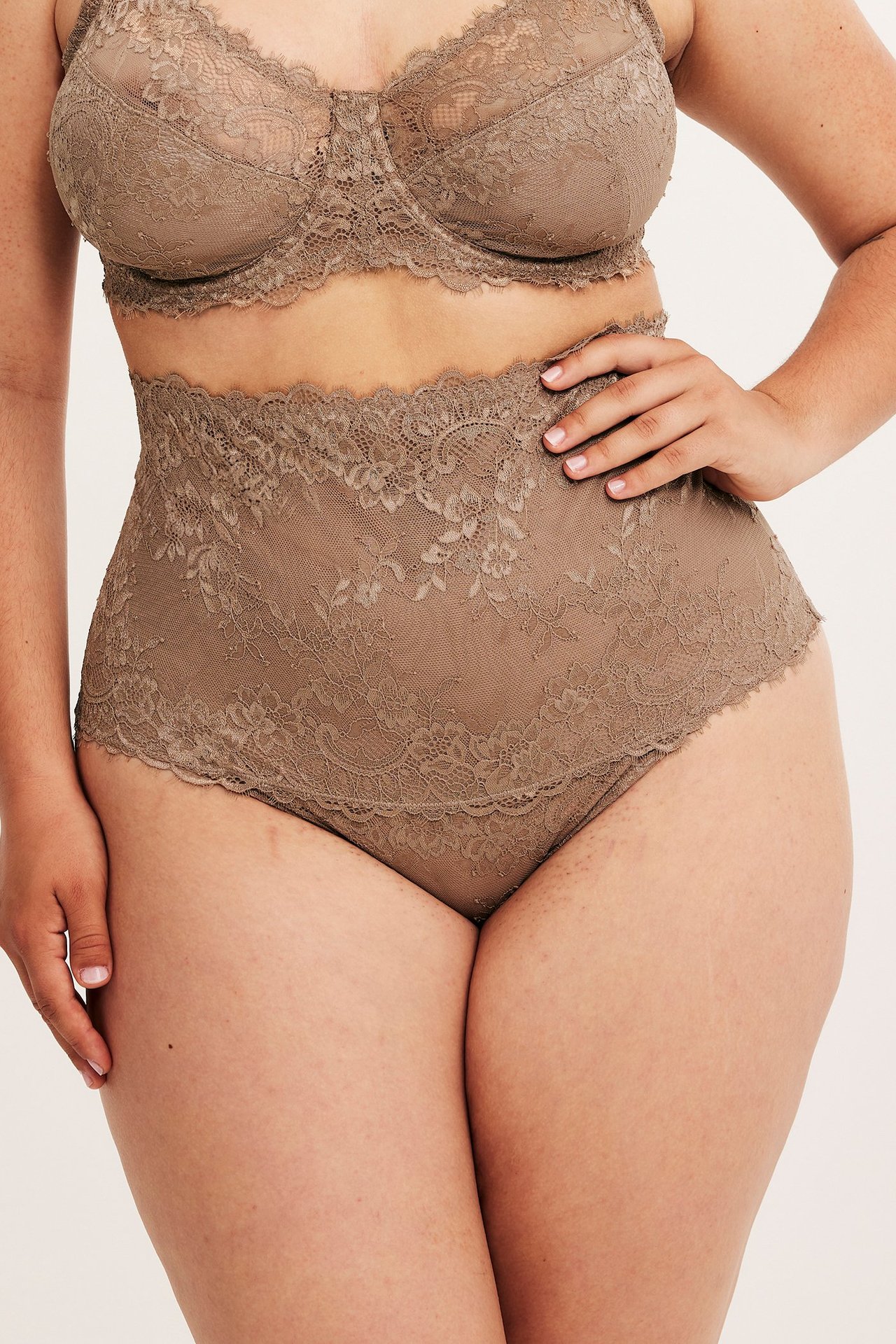 Framifrån, kvinna i beige högmidjad spetstrosa i stringmodell och matchande spets-bh.