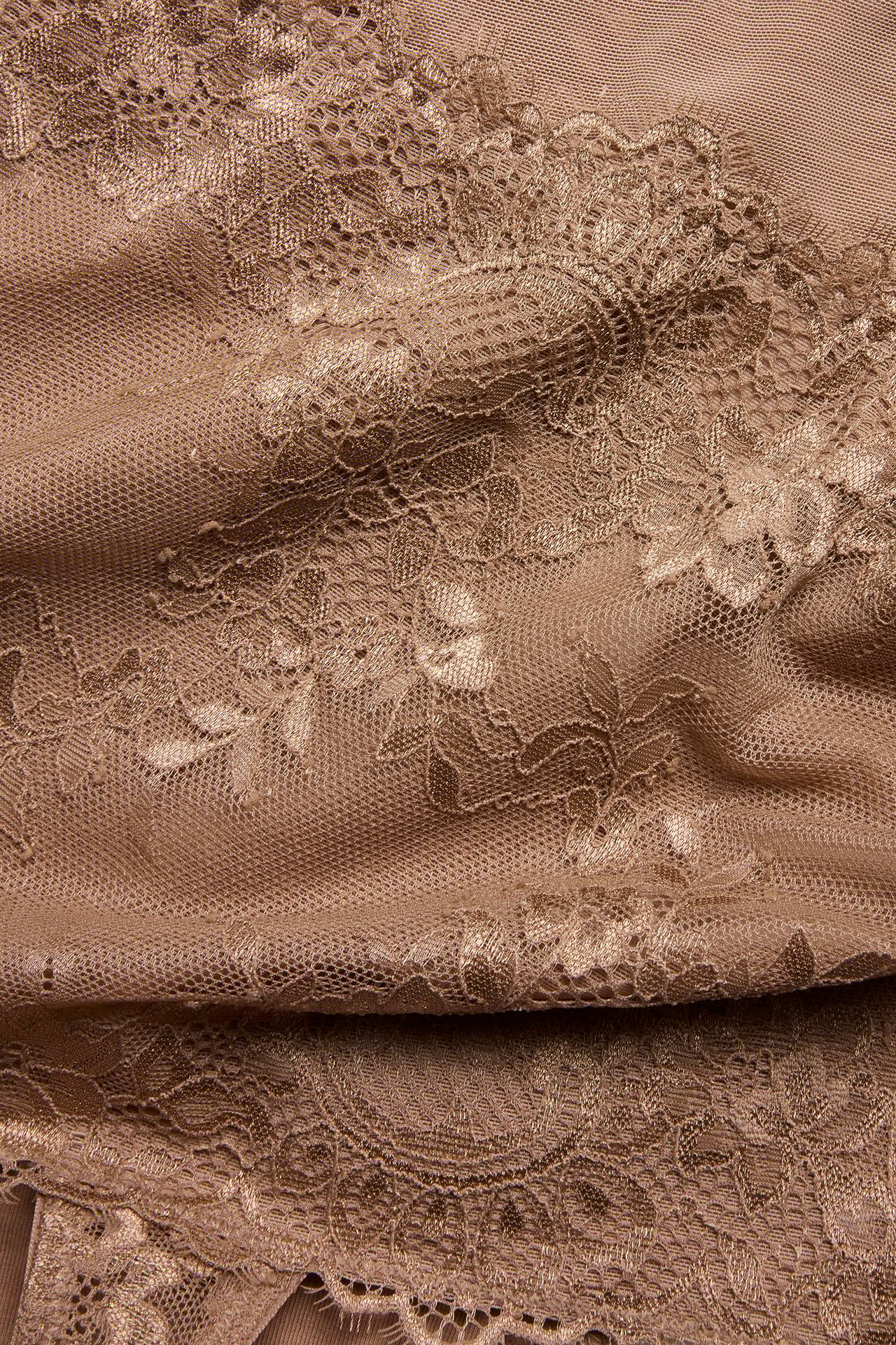 Zbliżenie beżowego koronkowego materiału stringów, z misternym kwiatowym wzorem.