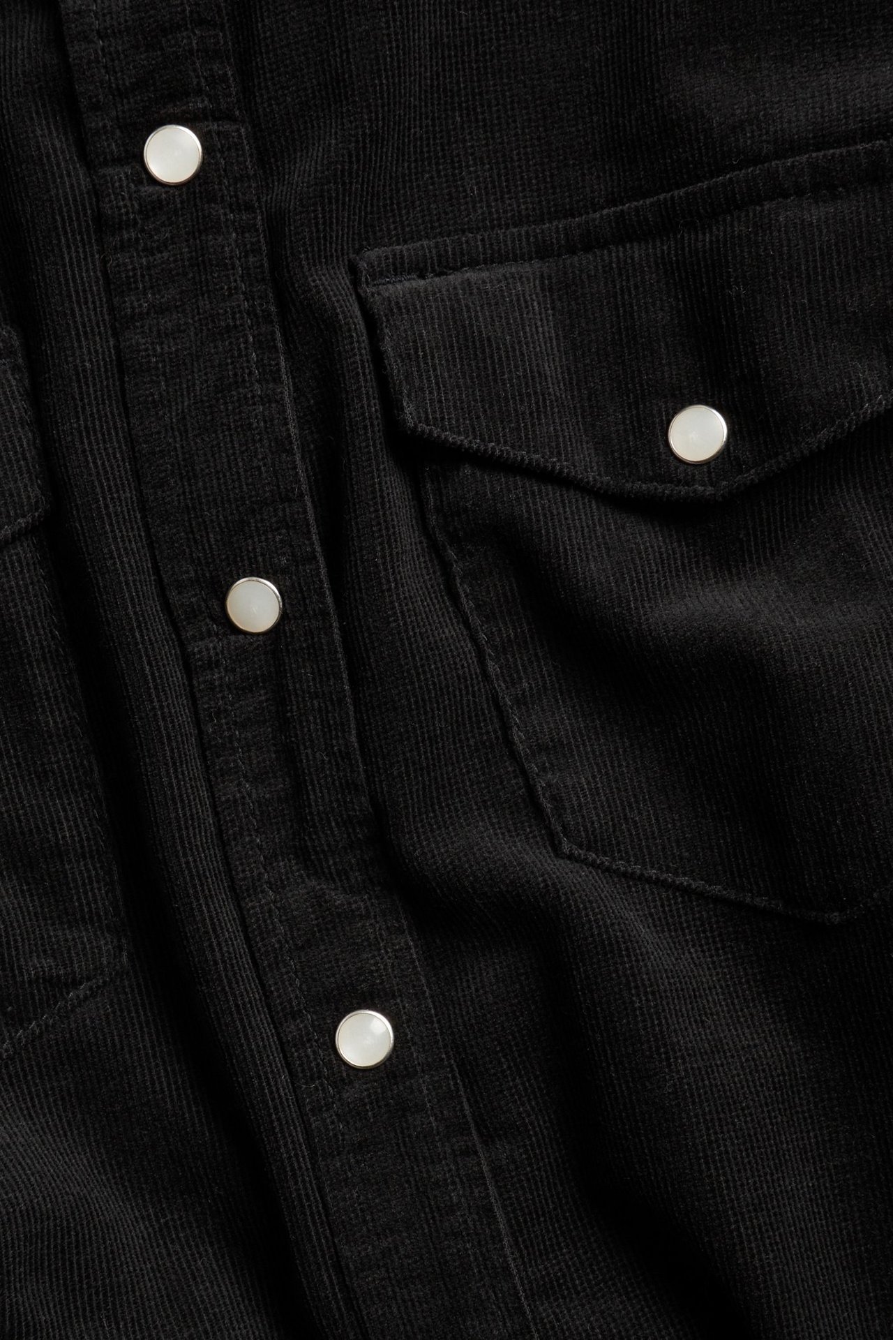 Zbliżenie czarnej koszuli sztruksowej z białymi zatrzaskami i dwiema kieszeniami na piersi.