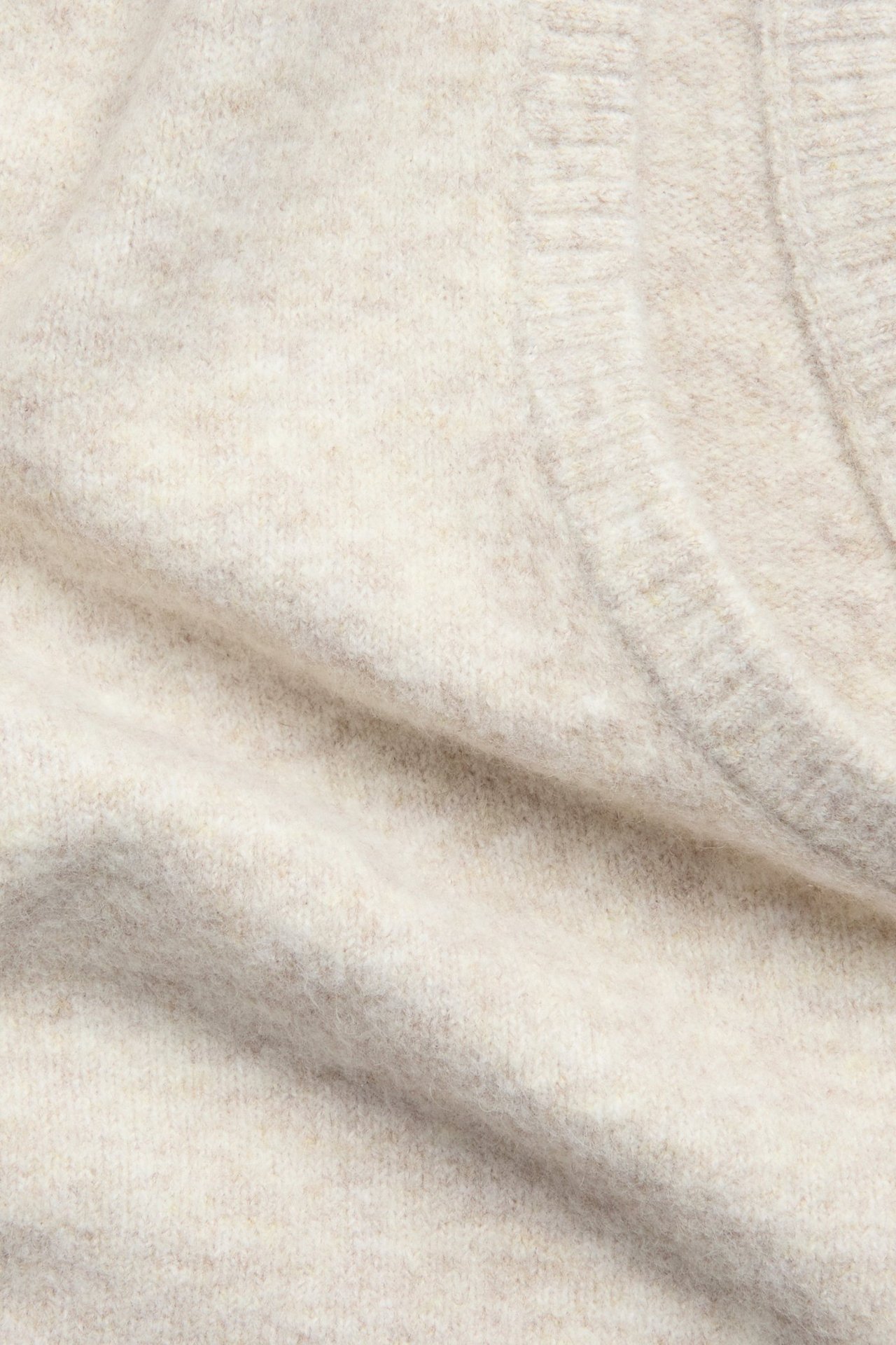 Zbliżenie jasnobeżowej melanżowej dzianiny kamizelki, ukazujące jej miękką teksturę.