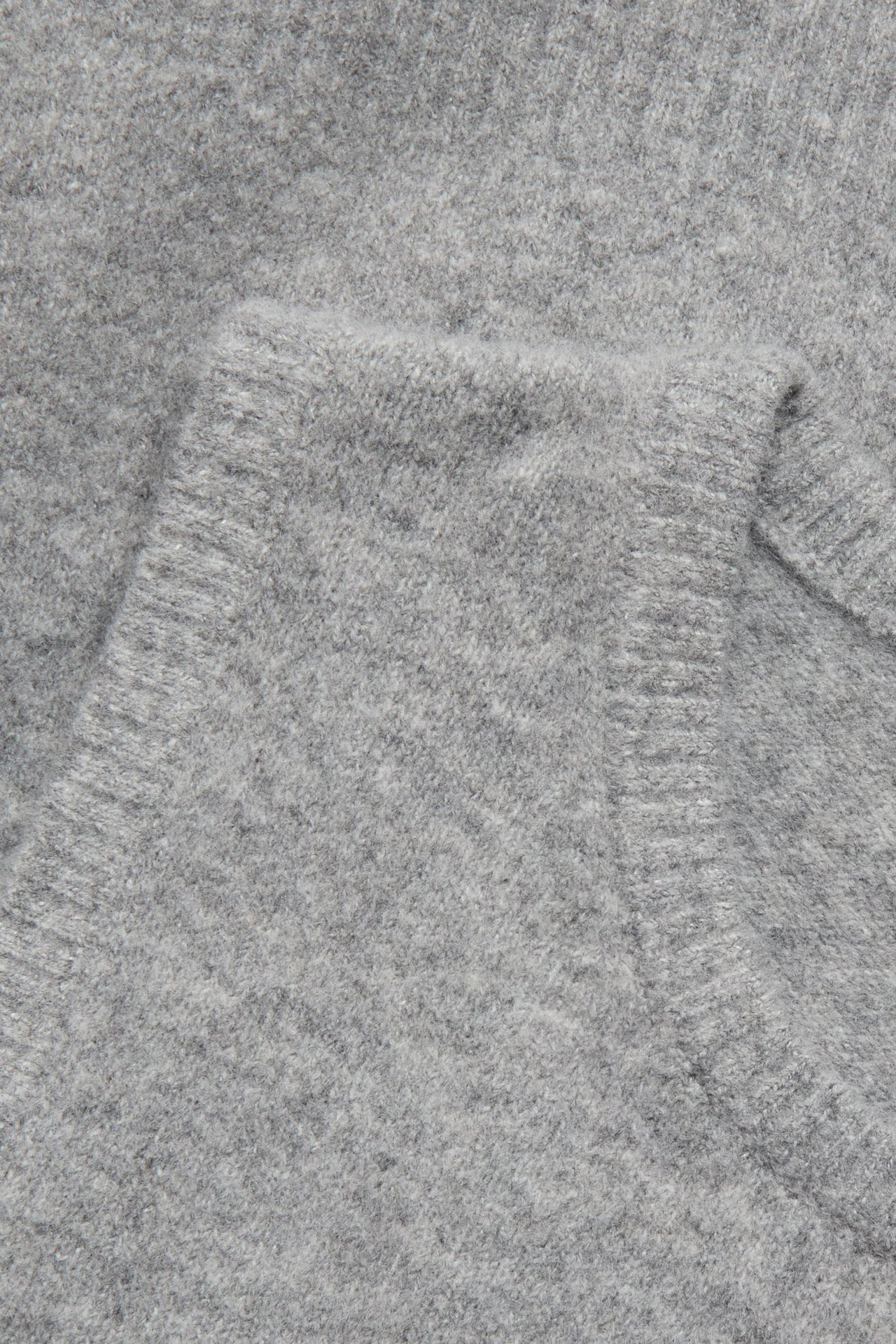 Zbliżenie jasnoszarej melanżowej kamizelki dzianinowej z miękkim, prążkowanym materiałem.