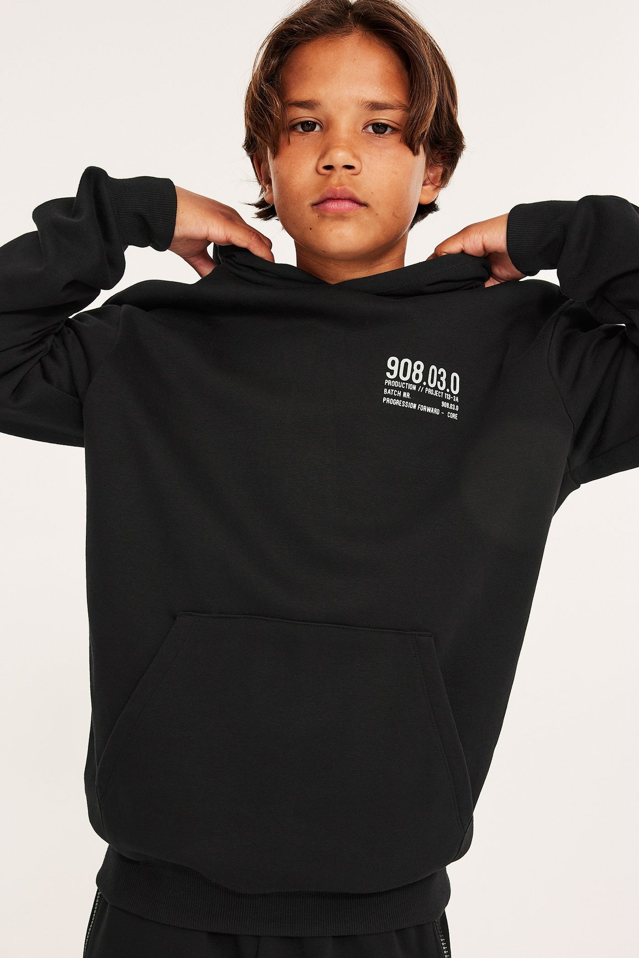 Widok z przodu: Dziecko w czarnej bluzie z kapturem, białym nadrukiem, kieszenią kangurką i ściągaczami.