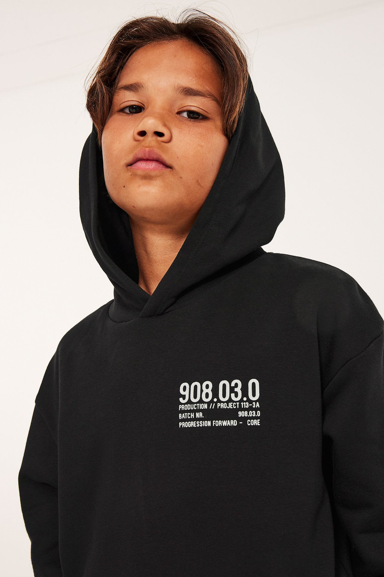 Närbild framifrån på ett barn i en svart hoodie med vitt texttryck på bröstet.