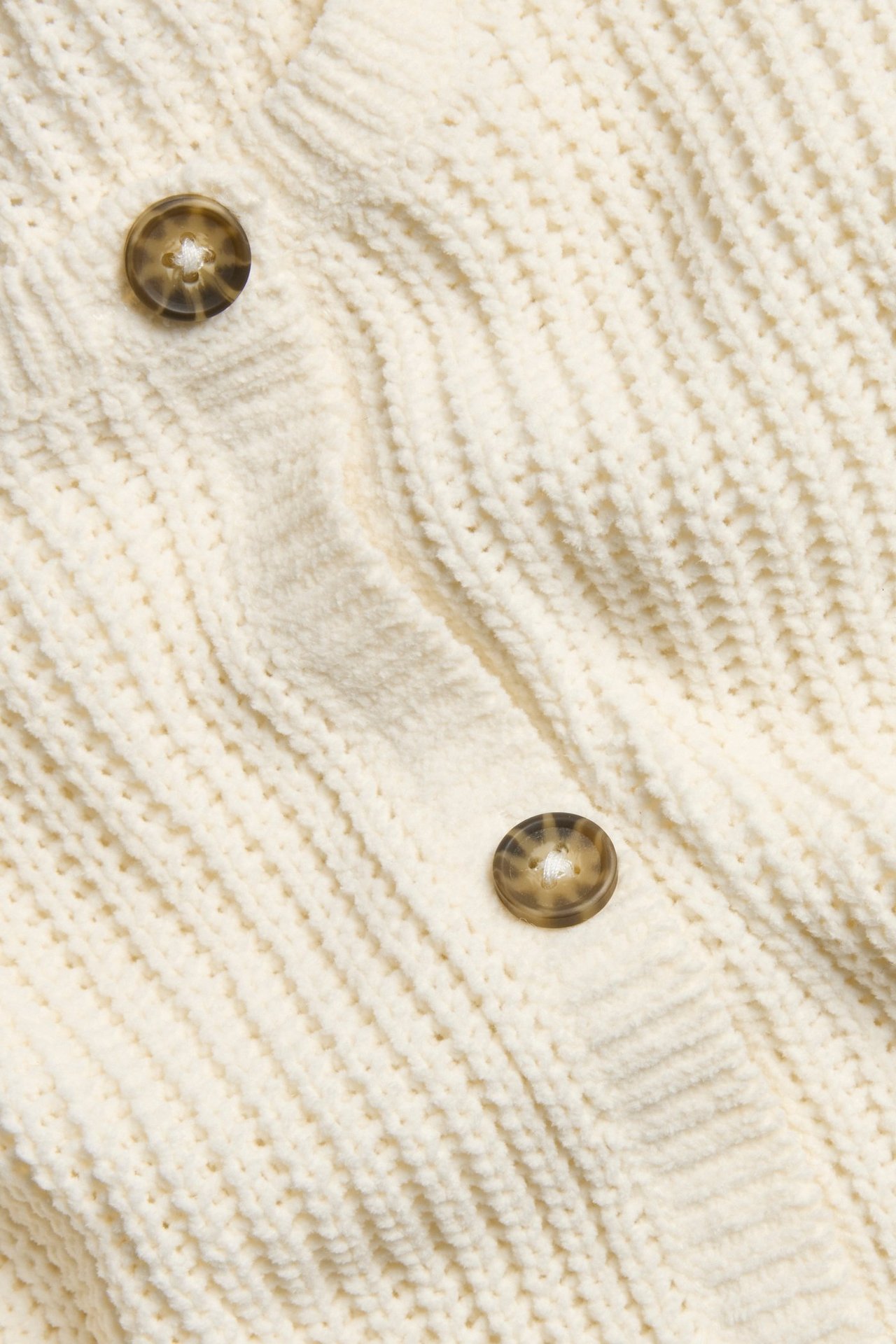 Zbliżenie białego, miękkiego swetra rozpinanego z dwoma brązowymi guzikami.