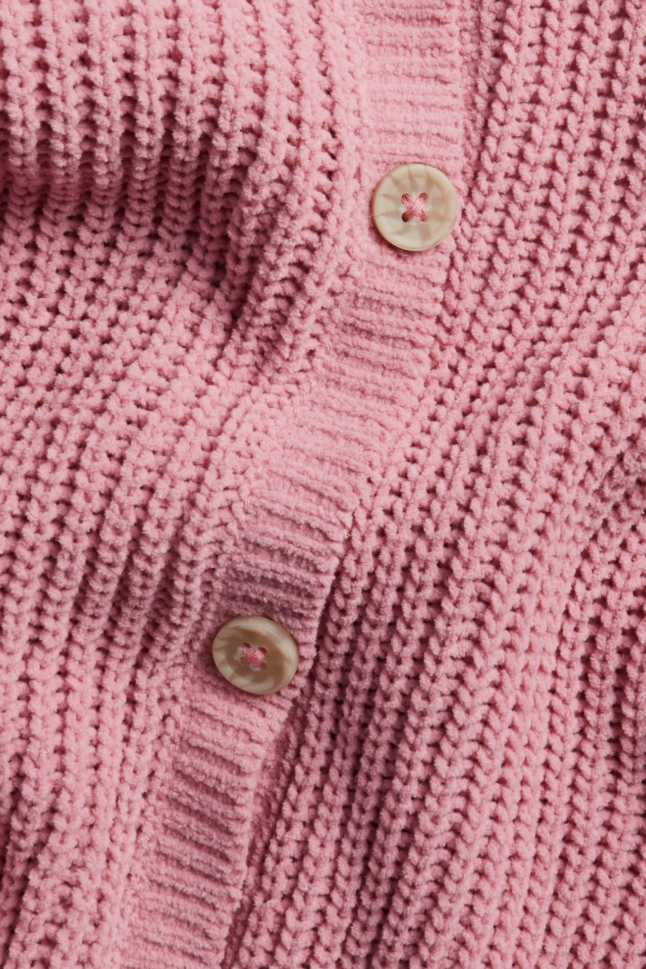 Zbliżenie różowego miękkiego swetra rozpinanego z dwoma jasnymi guzikami.