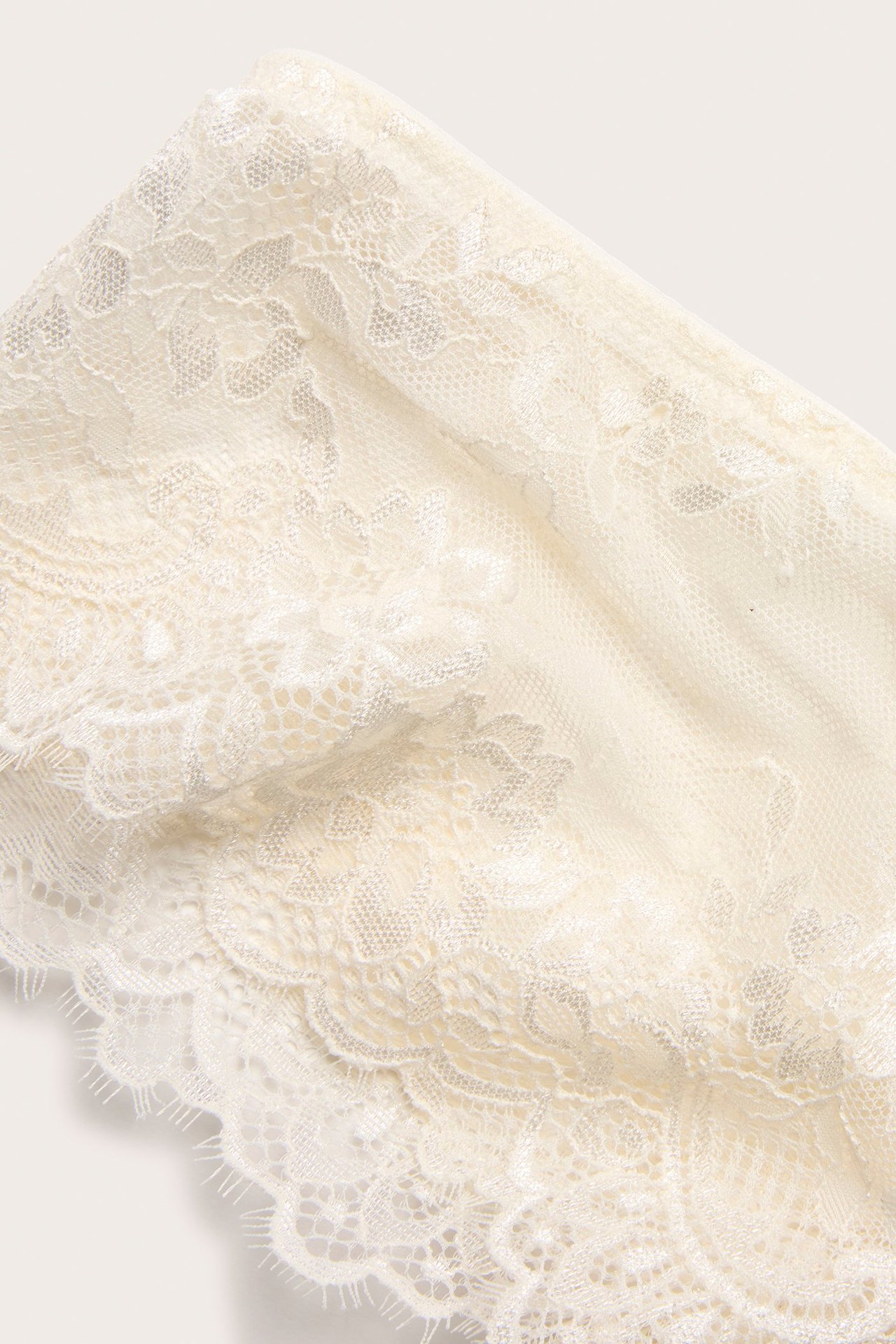 Zbliżenie na figi cheeky w kolorze ecru, z ozdobnej koronki z rzęskami i kwiatowym wzorem.