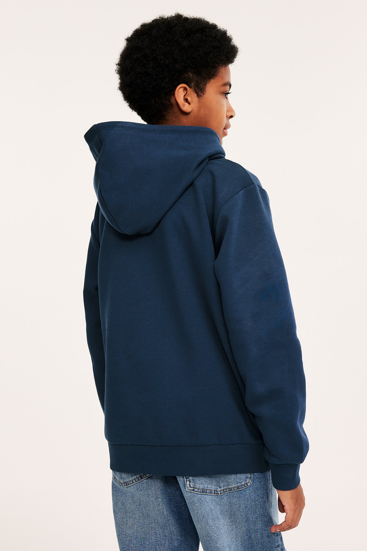Sidevisning av et barn i en mørkeblå hettegenser med hette og blå jeans.