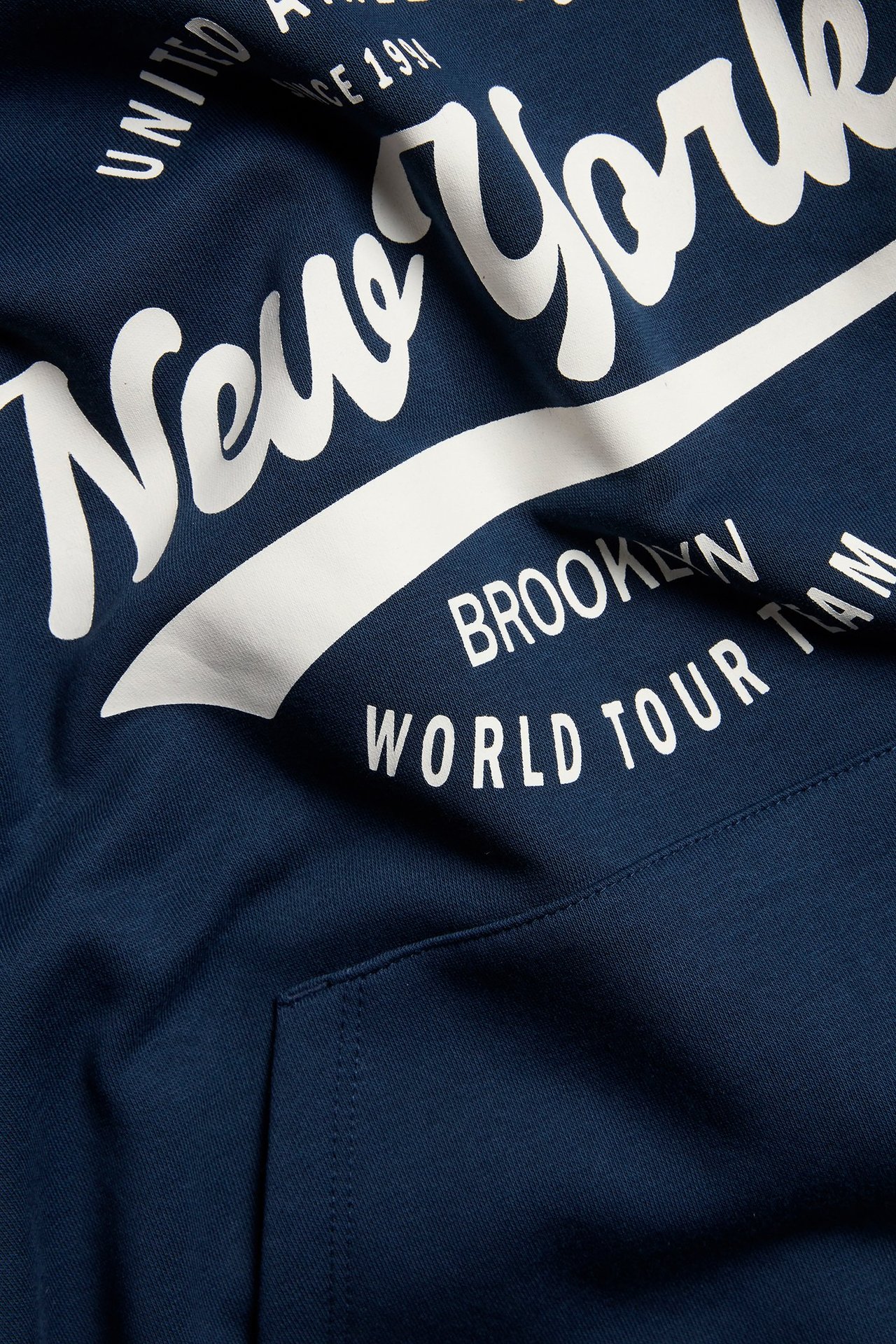 Zbliżenie na granatową bluzę dziecięcą z białym nadrukiem "New York" i kieszenią kangurką.