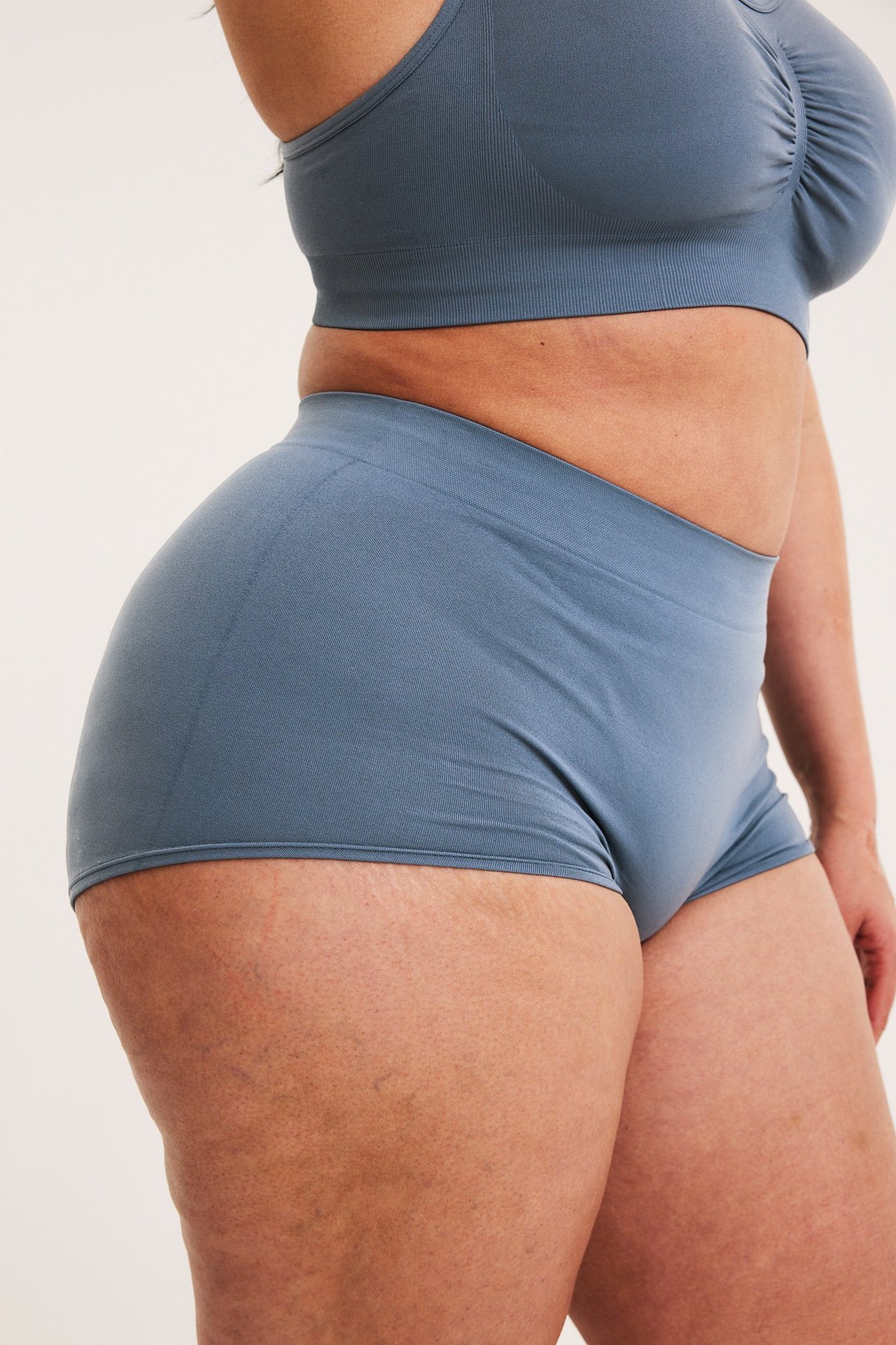 Widok z boku kobiety w ciemnoniebieskich bezszwowych bokserkach i pasującym biustonoszu.