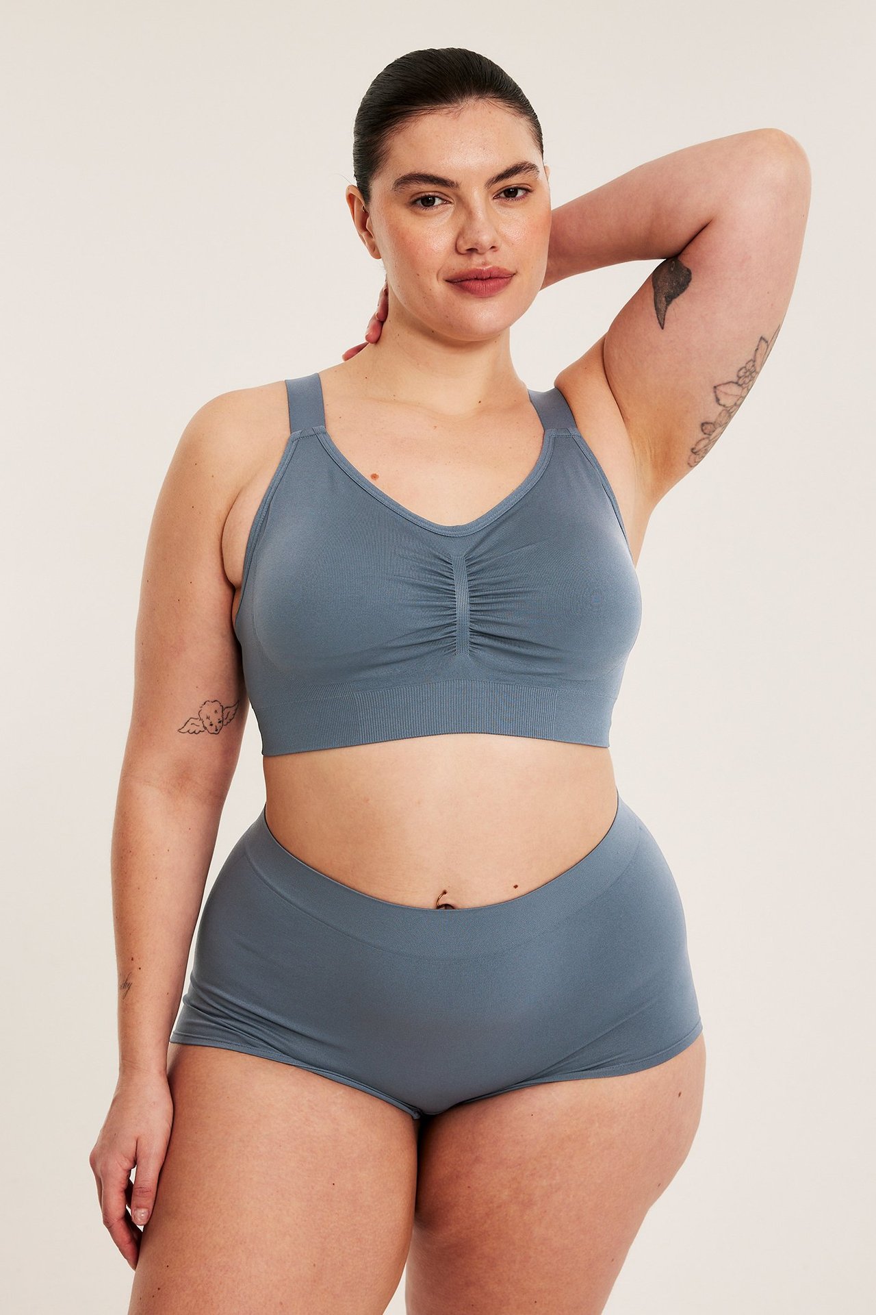 Edestäpäin nainen yllään tummansiniset saumattomat bokserialushousut ja yhteensopivat saumattomat rintaliivit.