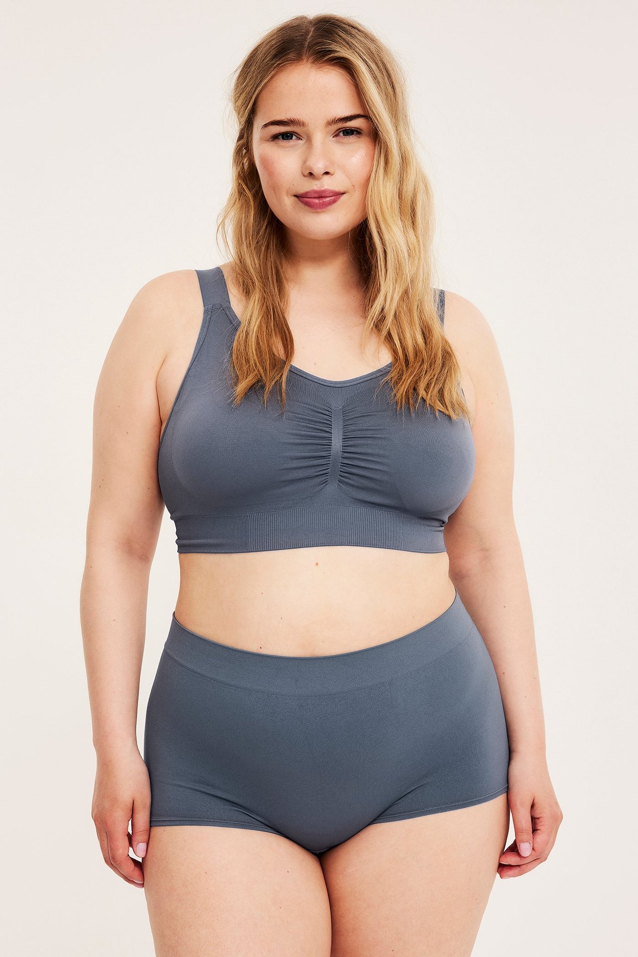 Frontbilde av en kvinne i mørkeblå sømløse boksershorts og en matchende sømløs BH.