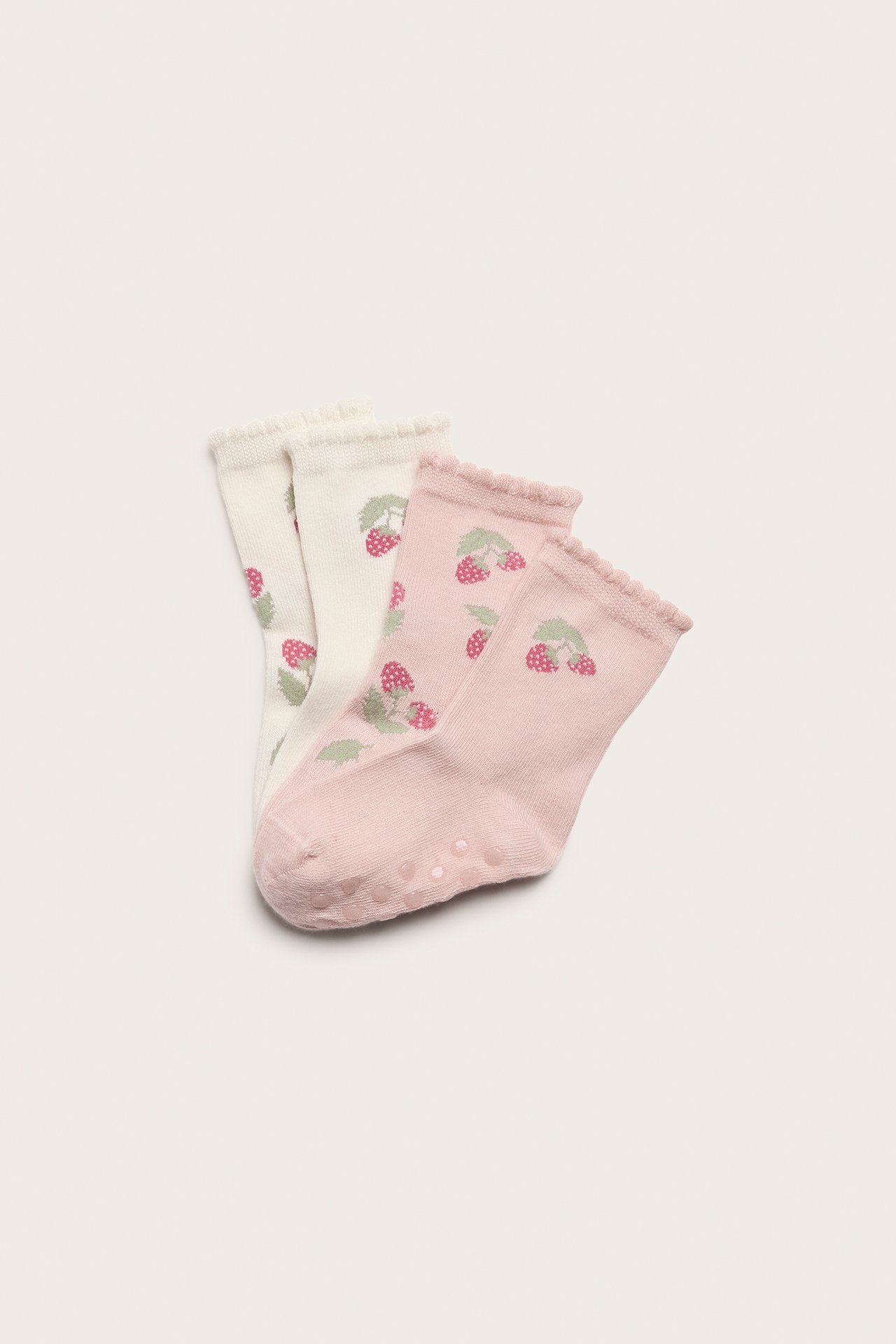 Ovanifrån: Fyra babystrumpor, två offwhite, två rosa, med jordgubbsmönster, uddkant och antislip.