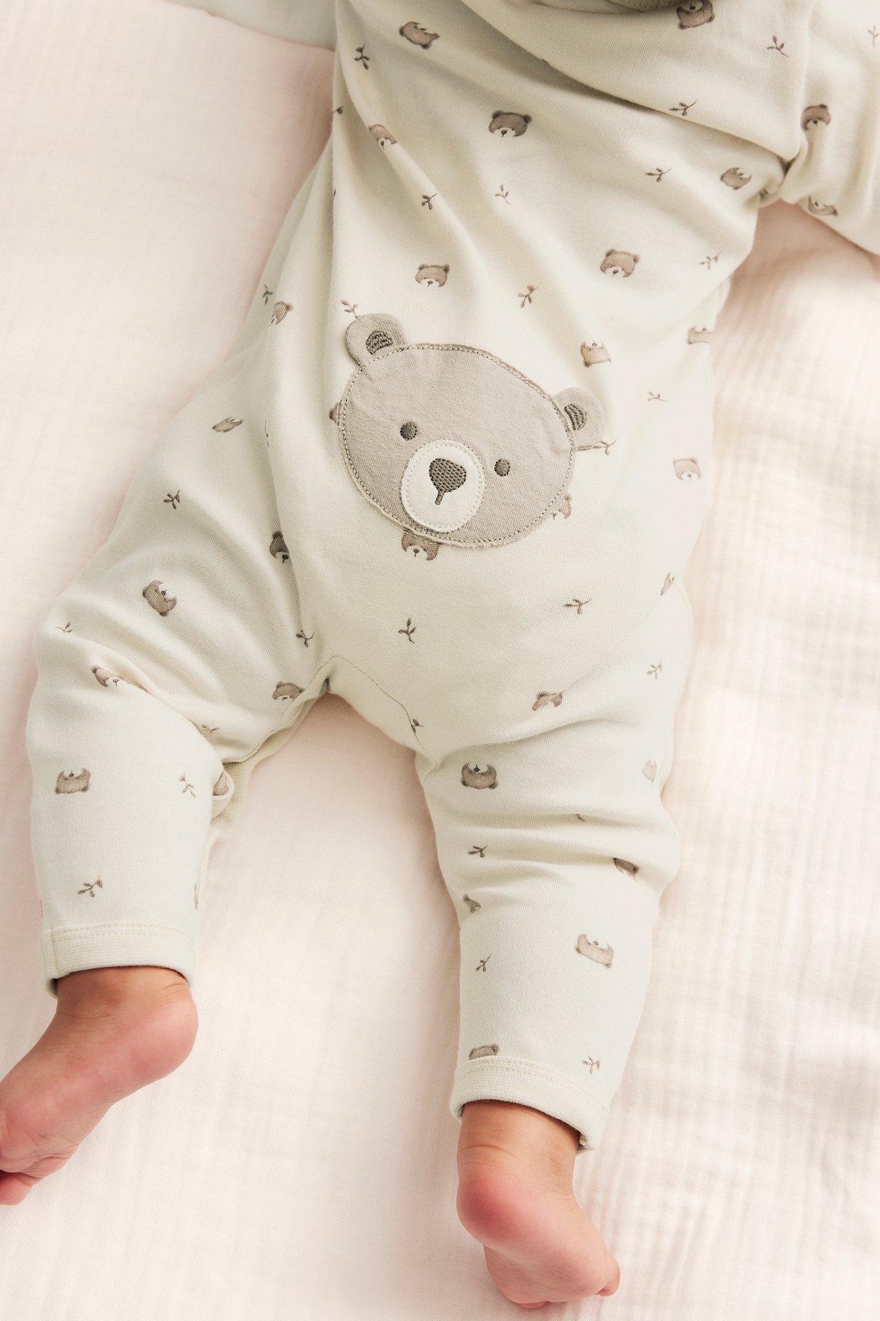 Lähikuva vauvasta vaaleanbeigessä puuvillapyjamassa, jossa ruskea nallekuvio ja harmaa nallesovellus.