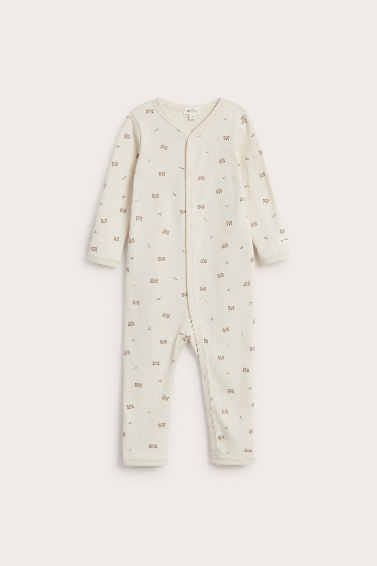 Edestä kuvattu vaaleanbeige vauvan puuvillapyjama pienellä nallekuviolla ja painonapeilla.