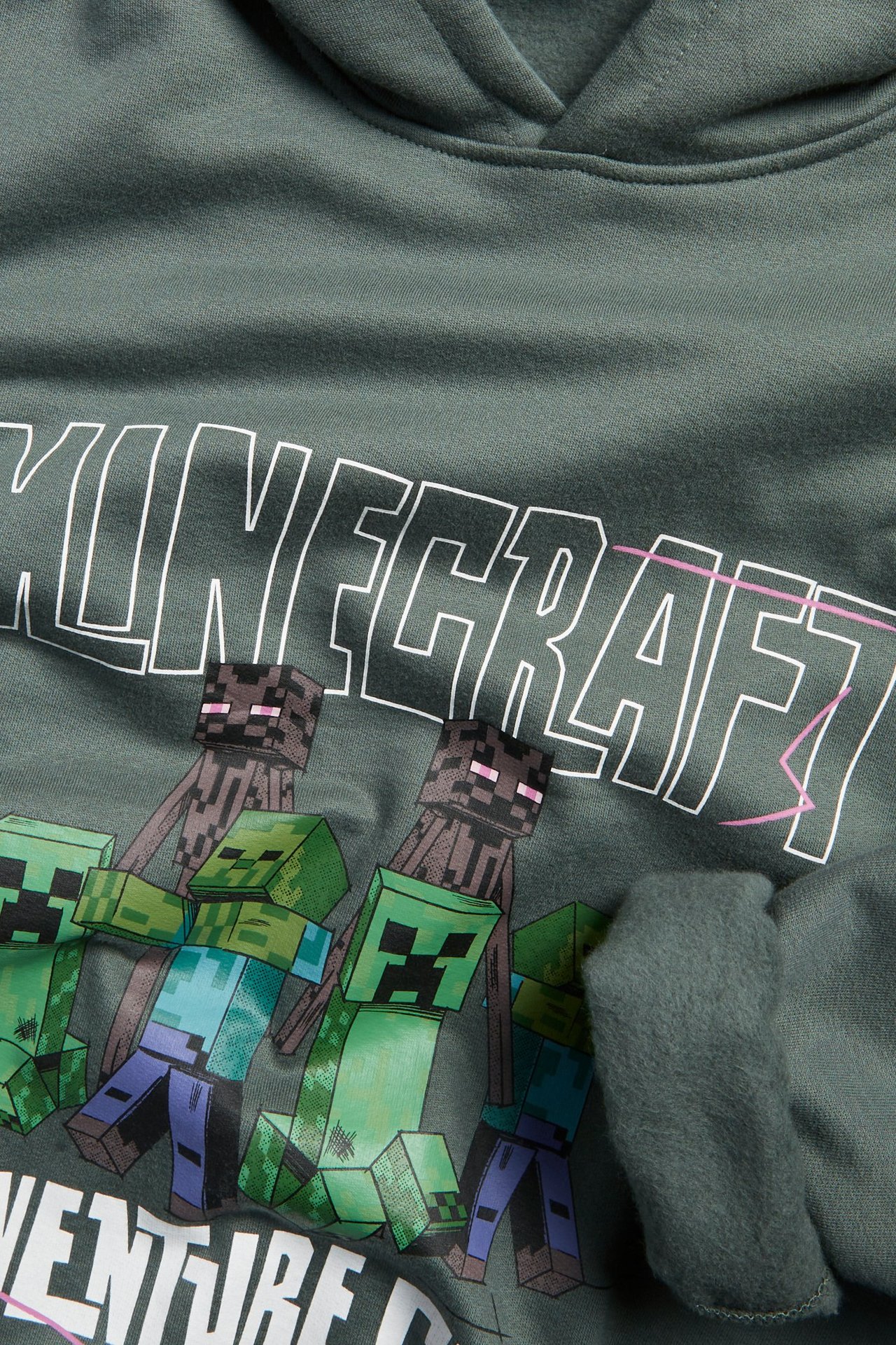 Nærbilde av en khakigrønn barnehettegenser i bomull med børstet innside og 'Minecraft'-trykk.