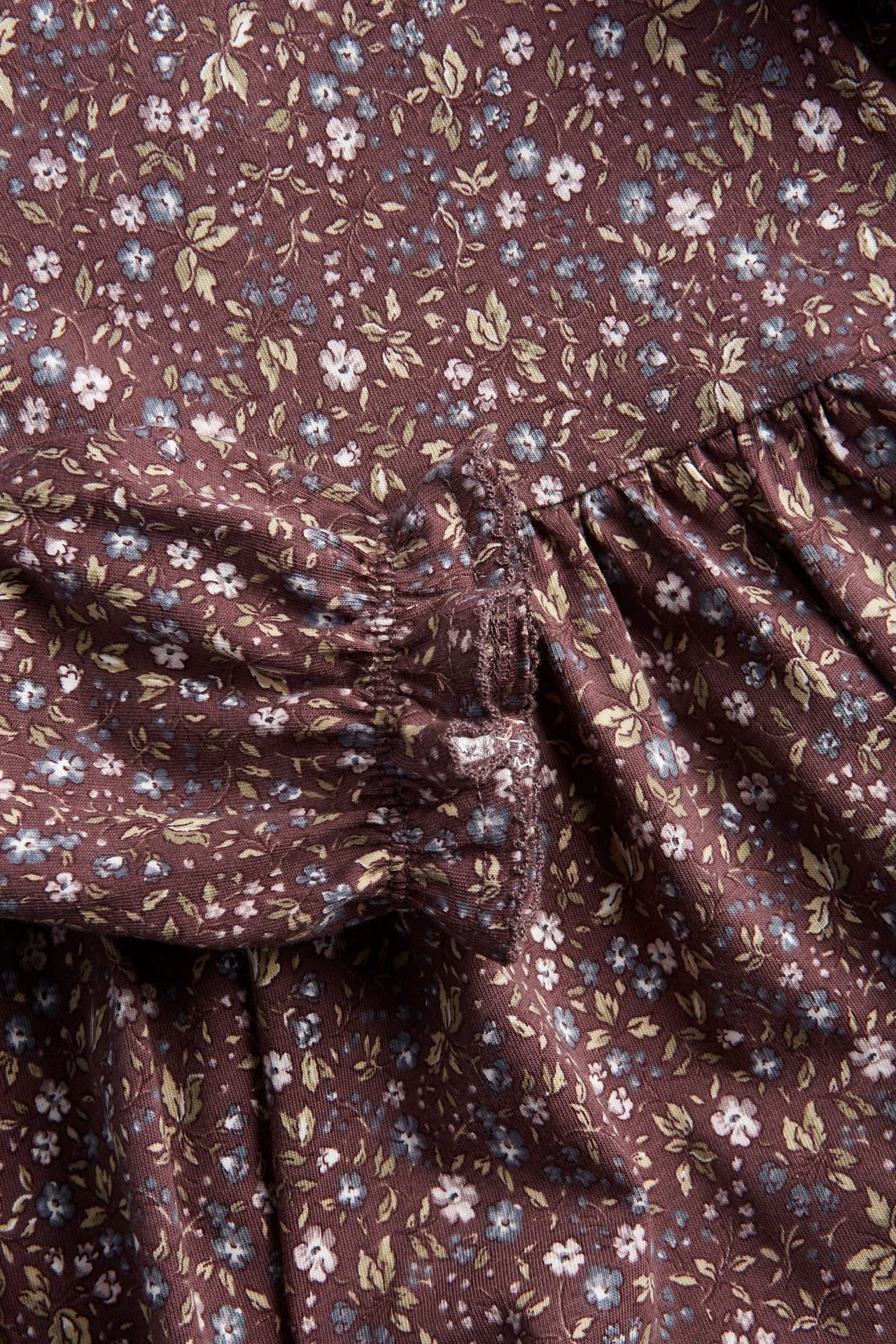 Zbliżenie na ciemnofioletową kwiecistą sukienkę dżersejową z marszczonym bufiastym rękawem i elastycznym mankietem.