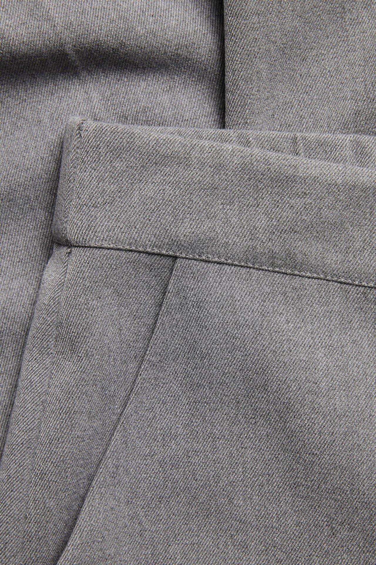 Zbliżenie jasnoszarych spodni garniturowych o melanżowym wzorze, pokazujące pas i kieszeń.