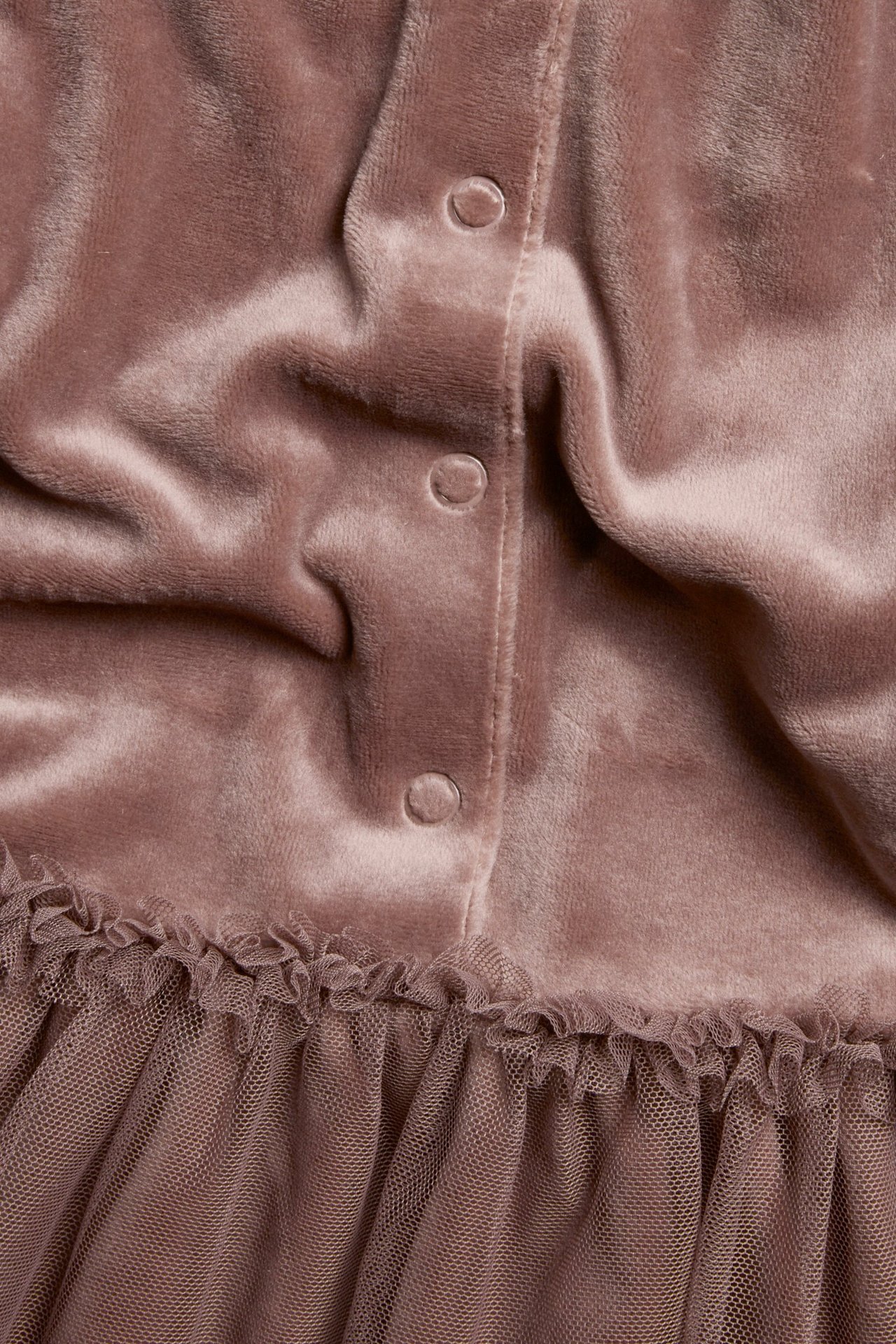 Zbliżenie ciemnoróżowej welurowej sukienki z zatrzaskami i falbankową tiulową spódnicą.