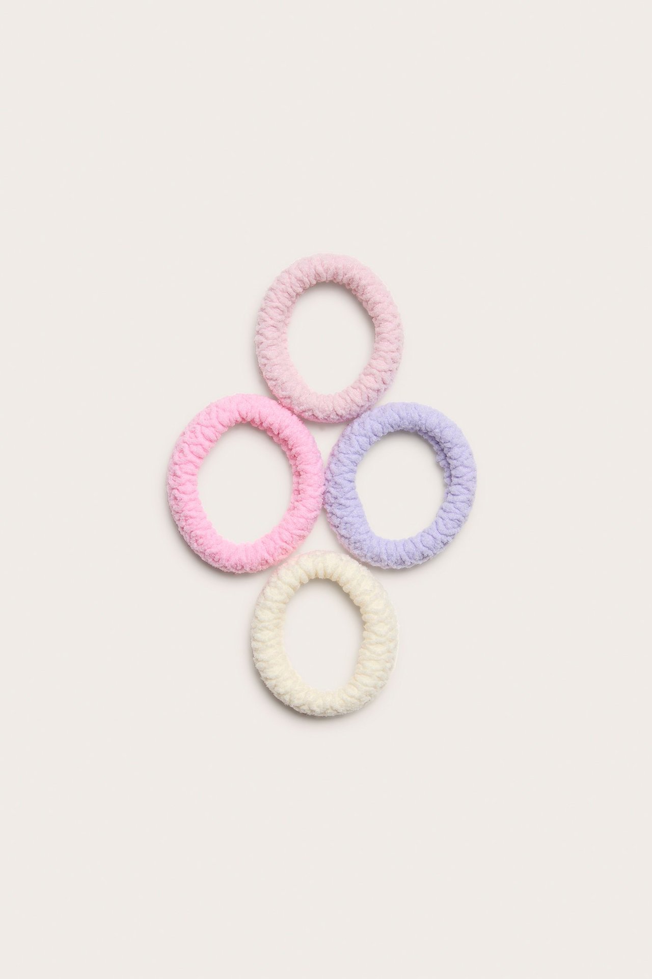 Widok z góry na cztery gumki do włosów z dżerseju w jasnoróżowym, różowym, jasnofioletowym i kremowym kolorze.
