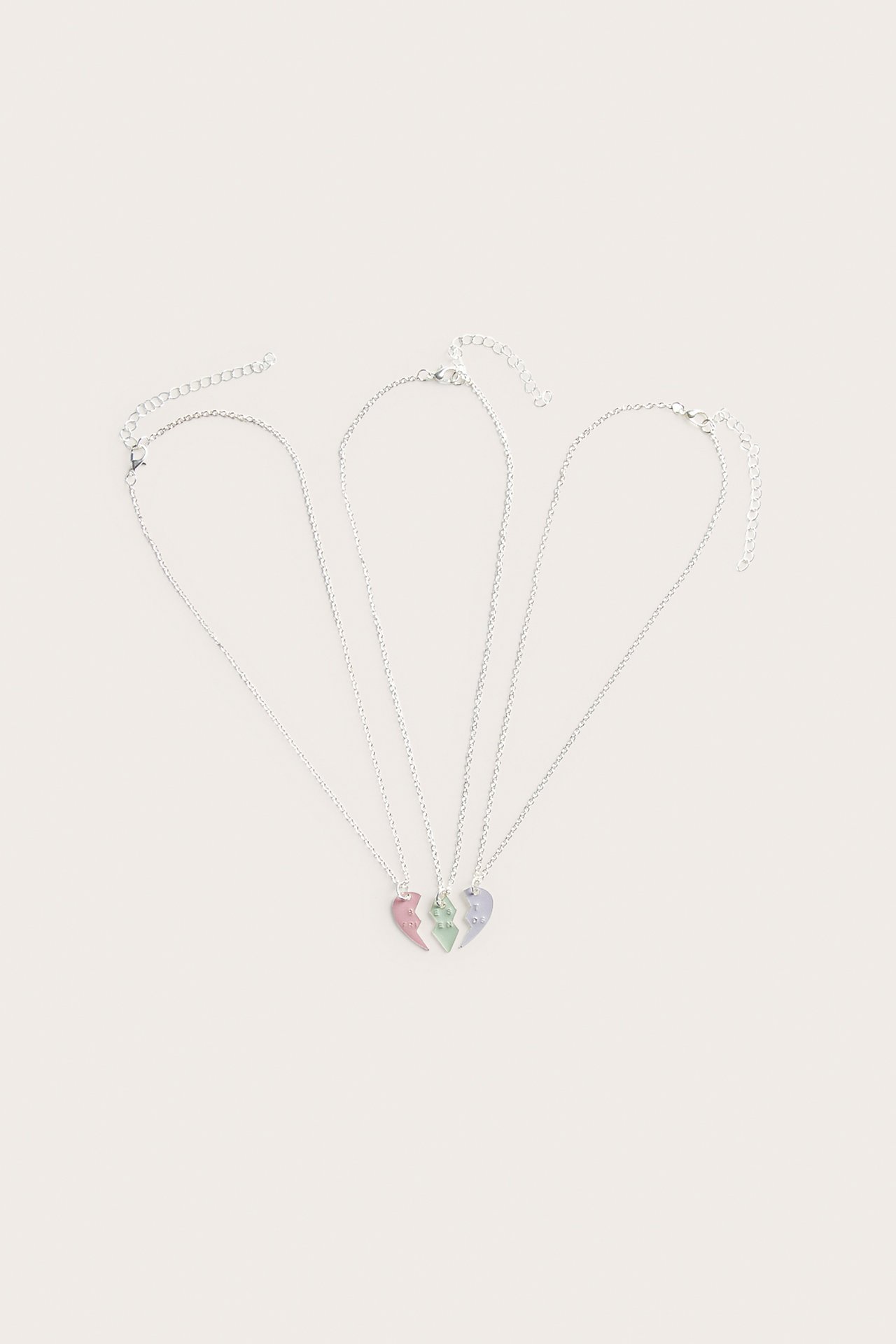 Platt liggande bild av tre silverhalsband med rosa, gröna och lila delade hjärtformade berlocker.