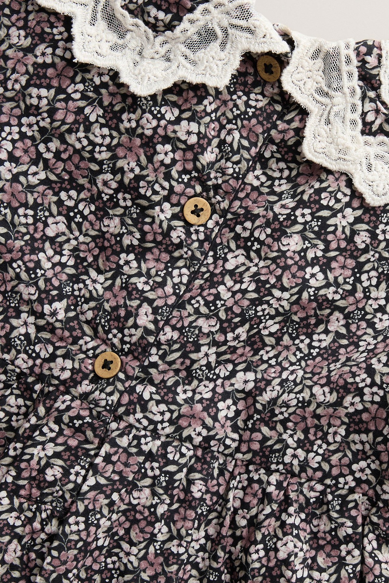Zbliżenie czarnej kwiecistej bawełnianej sukienki z białym koronkowym kołnierzem i drewnianymi guzikami.
