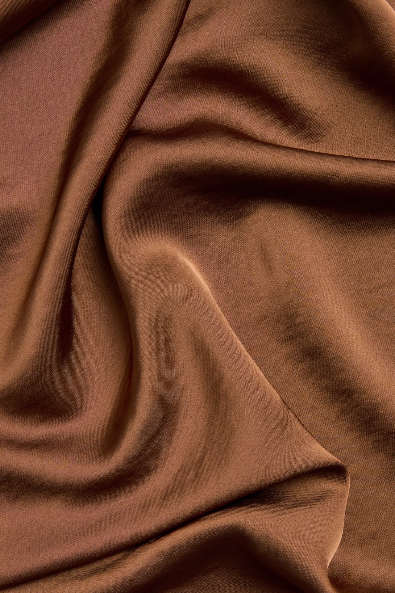 Zbliżenie brązowej, jednolitej tkaniny satynowej z miękkimi fałdami na spódnicę.