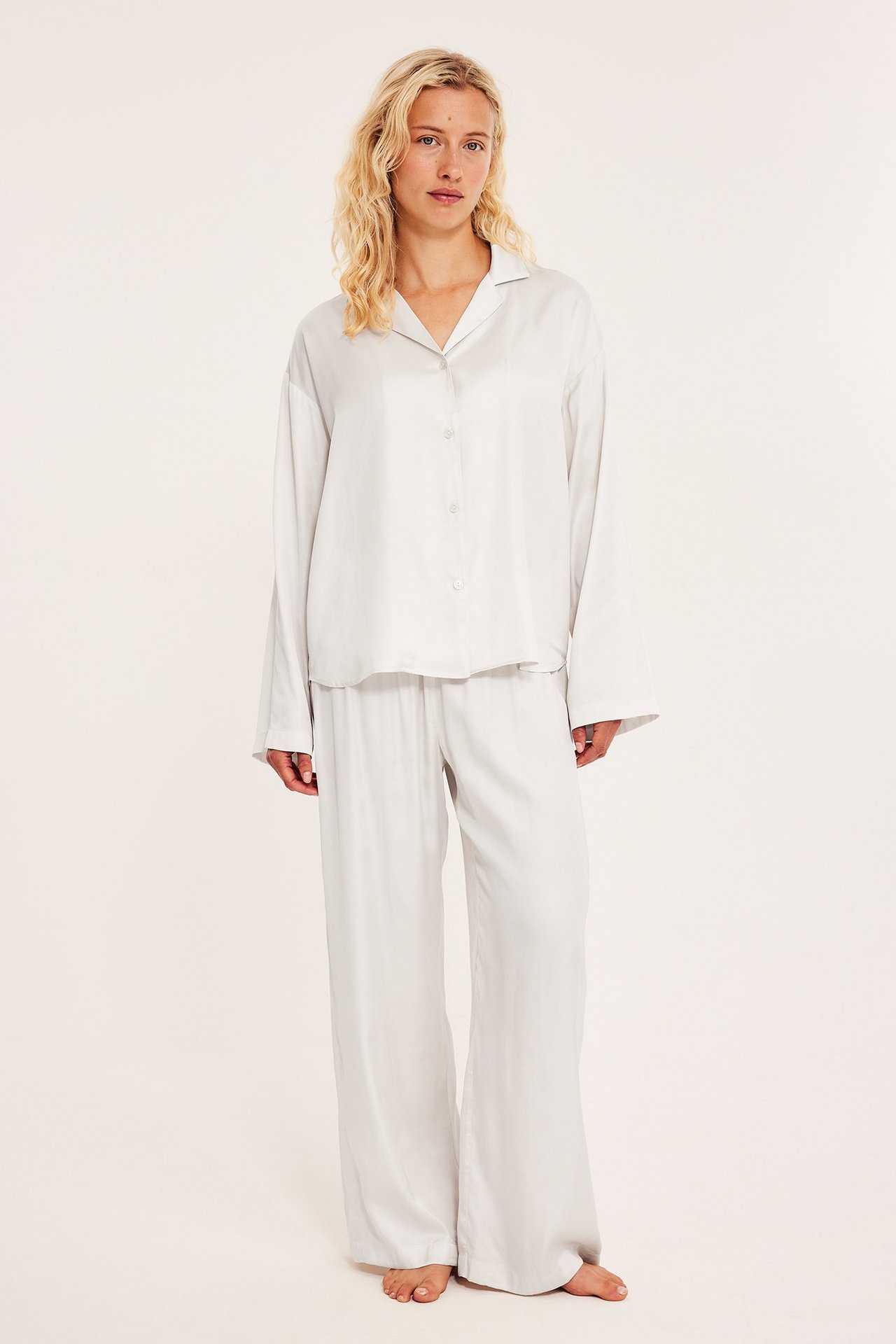 Framifrån, kvinna i avslappnad vit satinpyjamas: kragad topp, vida byxor.