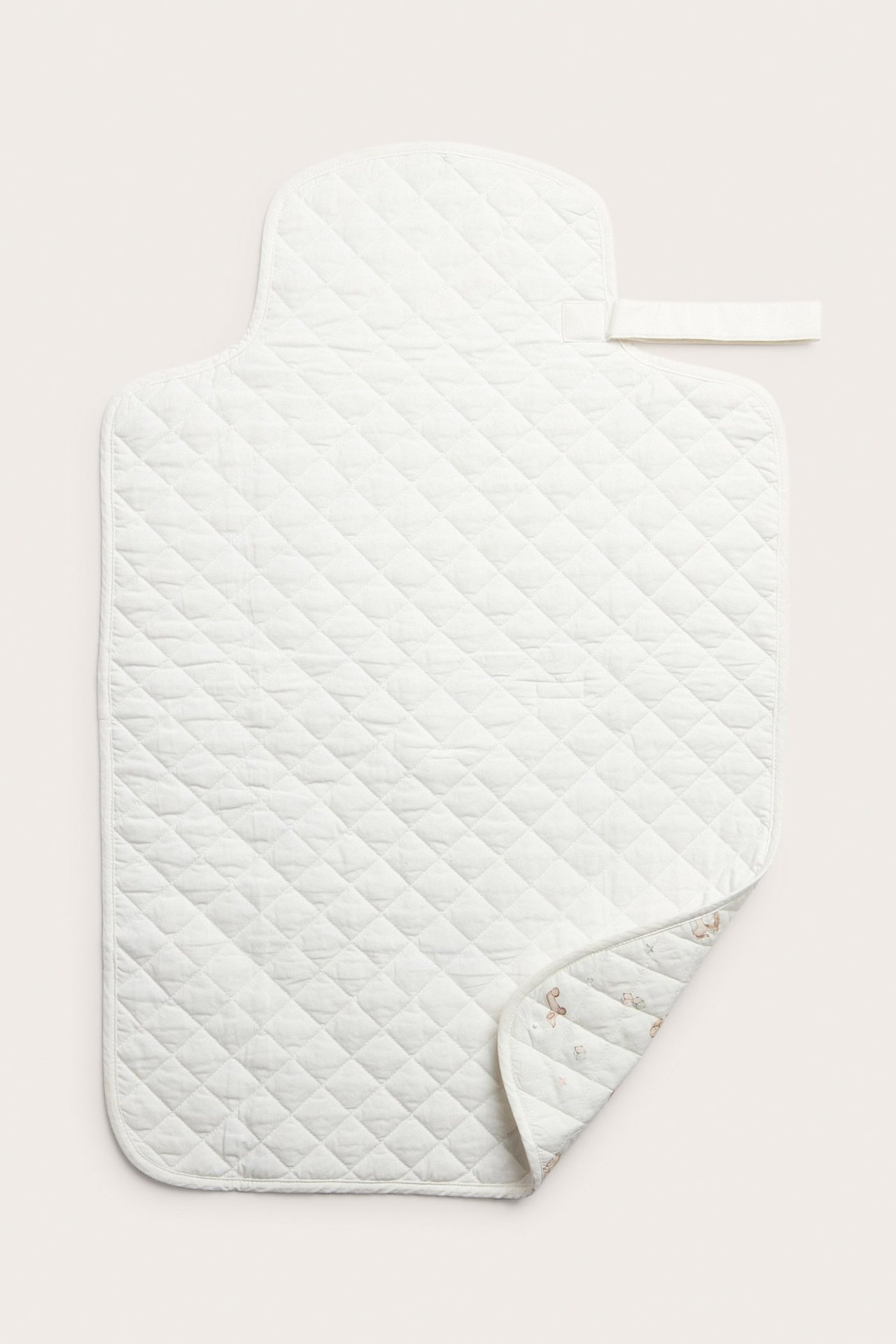 Ovanifrån: Offwhite quiltad vikbar skötbädd med handtag och mönstrad undersida.