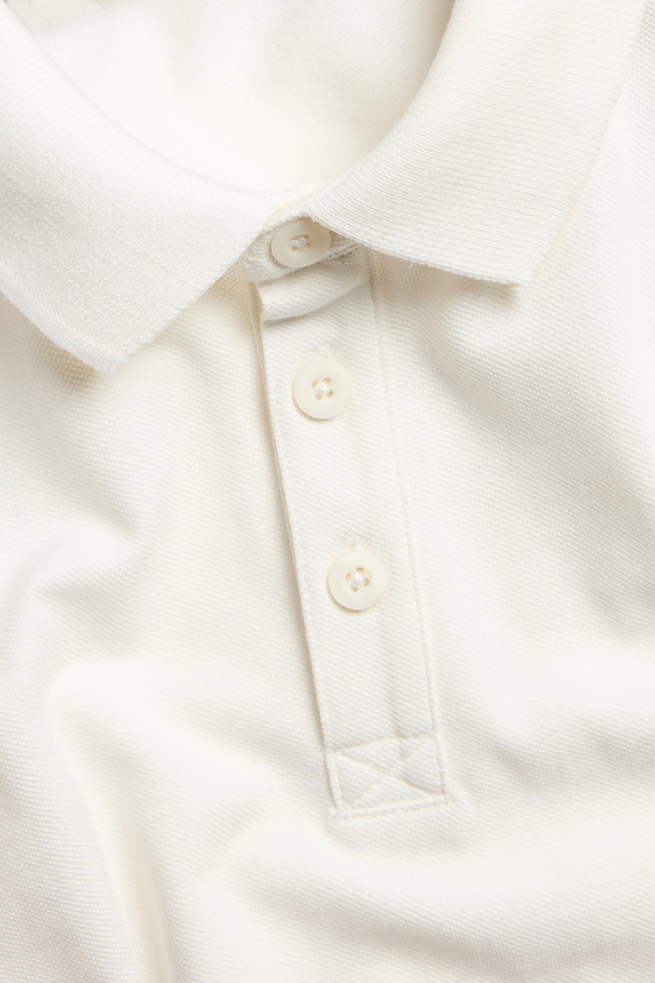 Zbliżenie na białą bawełnianą koszulkę polo z kołnierzykiem i listwą z trzema guzikami.