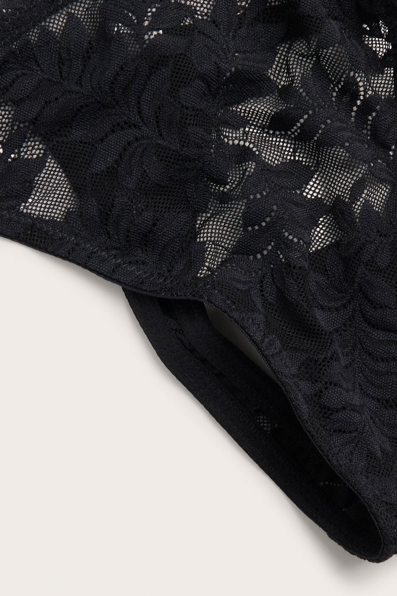 Zbliżenie czarnych, elastycznych koronkowych stringów z regulowanymi paskami bocznymi.