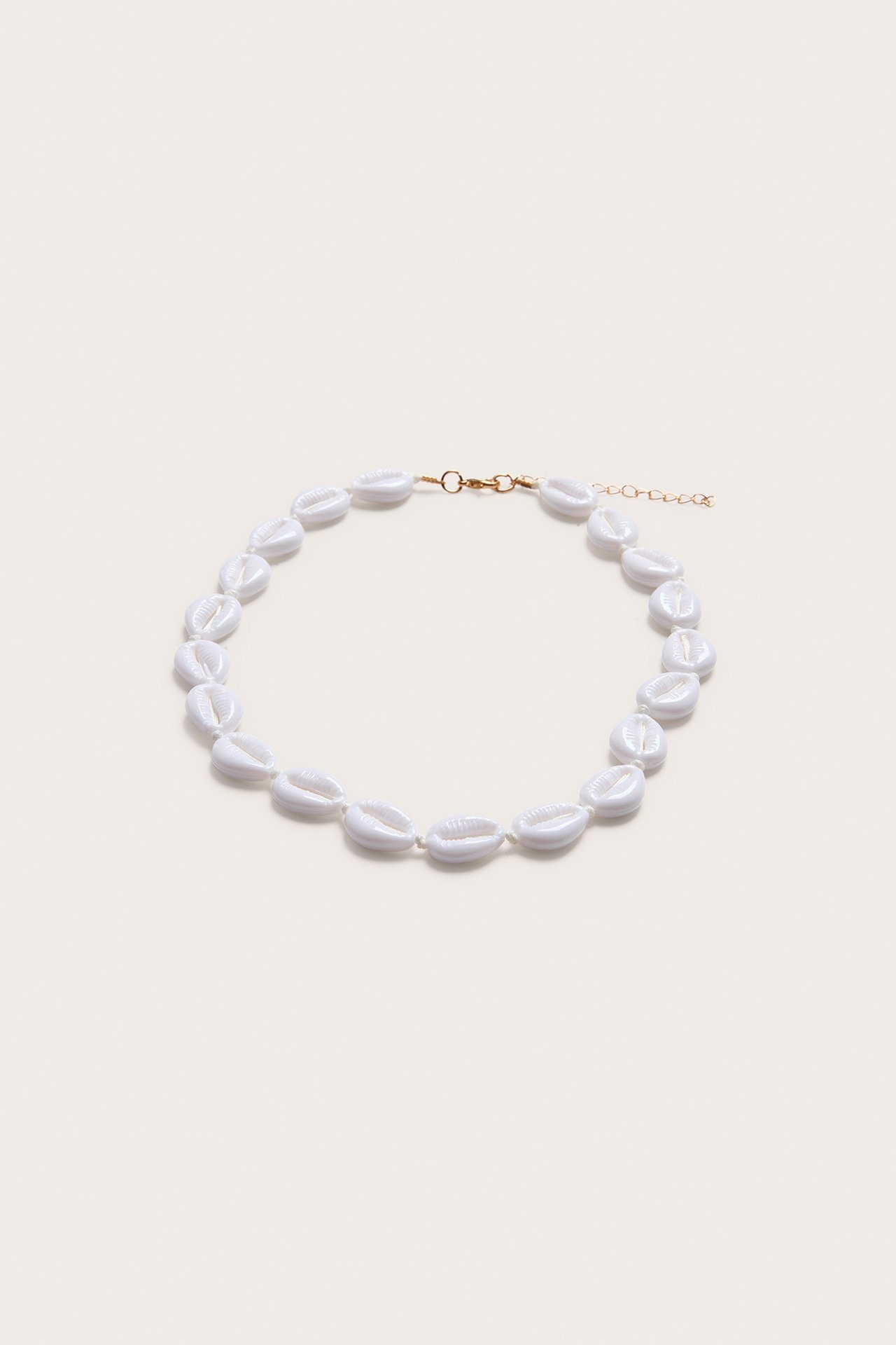 Närbild, uppifrån, av ett offwhite snäckhalsband med guldfärgat justerbart spänne.