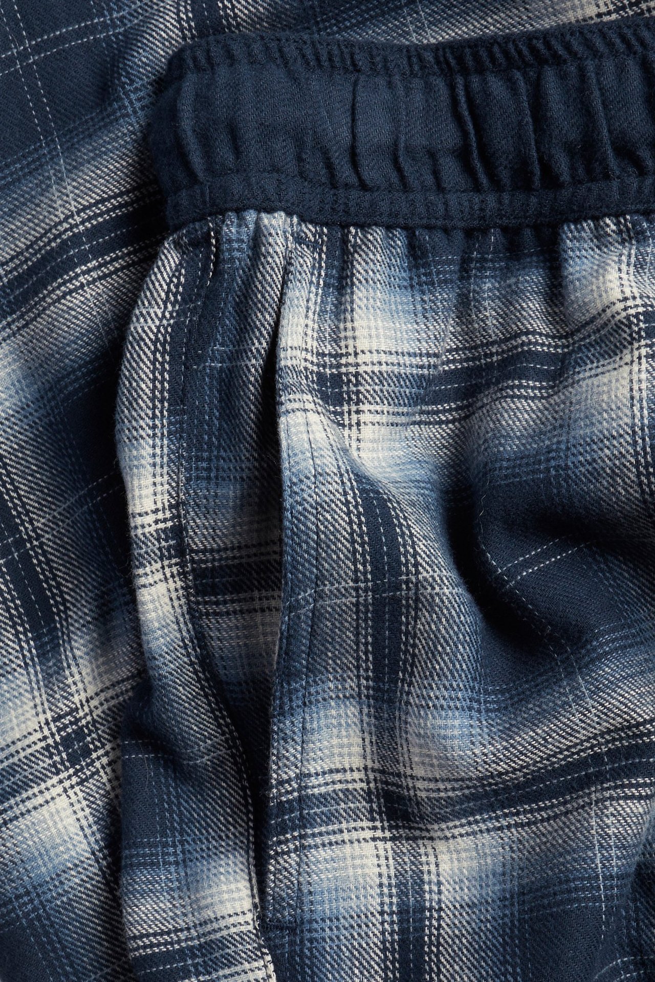 Zbliżenie na granatowe i białe spodnie flanelowe w kratę z elastycznym pasem i boczną kieszenią.