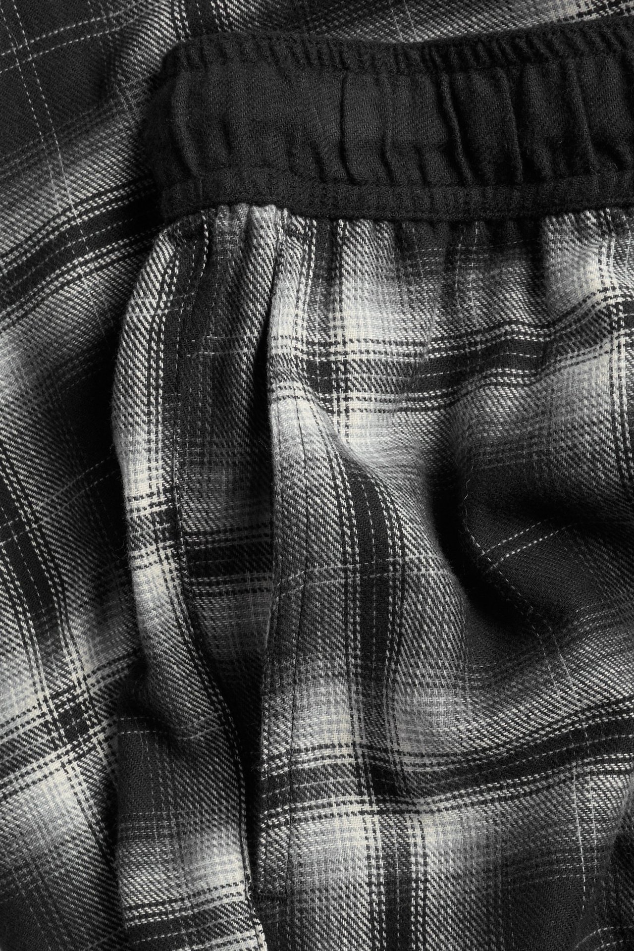 Zbliżenie męskich czarno-białych flanelowych spodni w kratę, z elastycznym pasem i kieszenią.