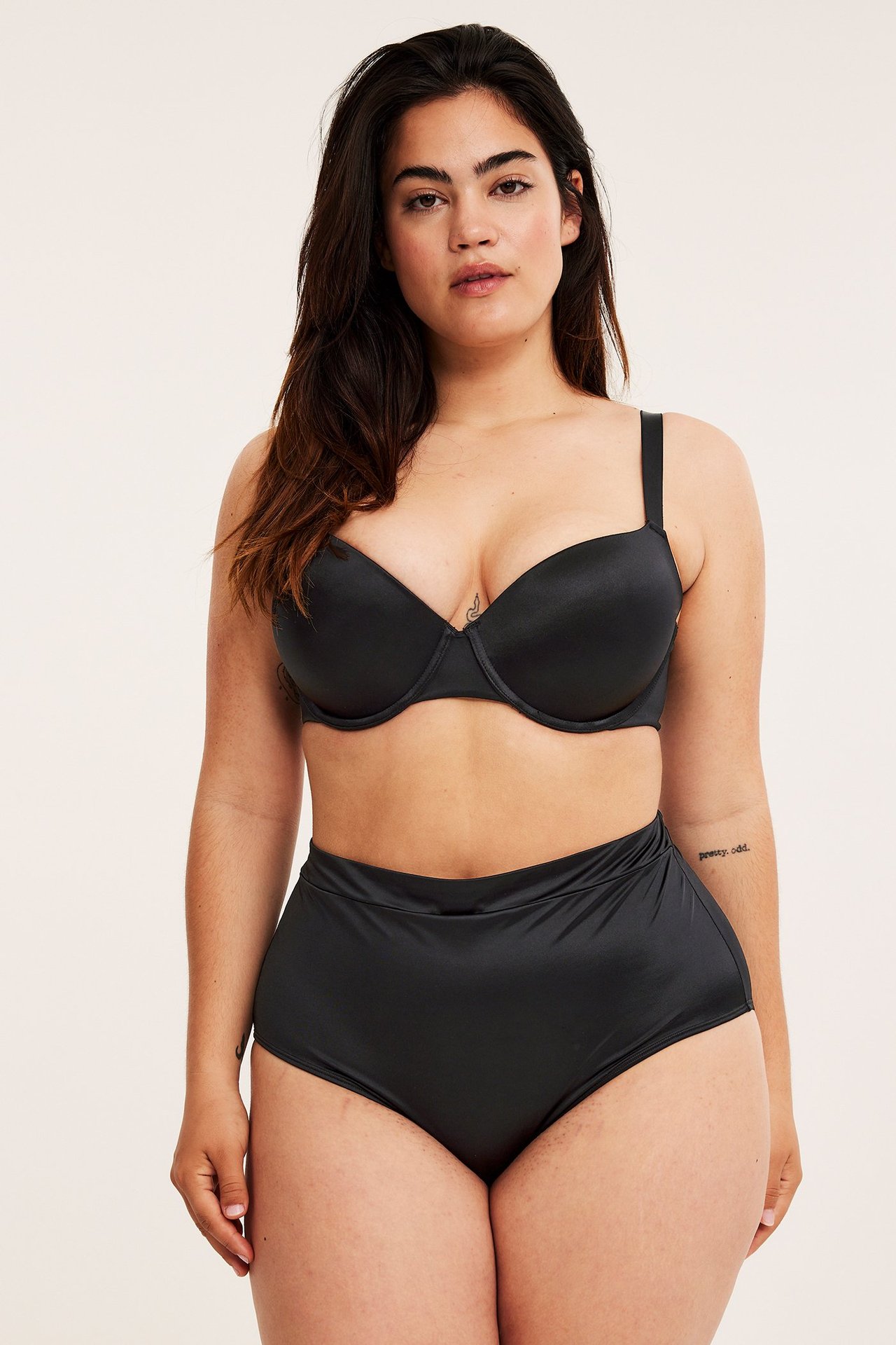 Forfra, kvinne i svarte høye glinsende truser og matchende svart BH.