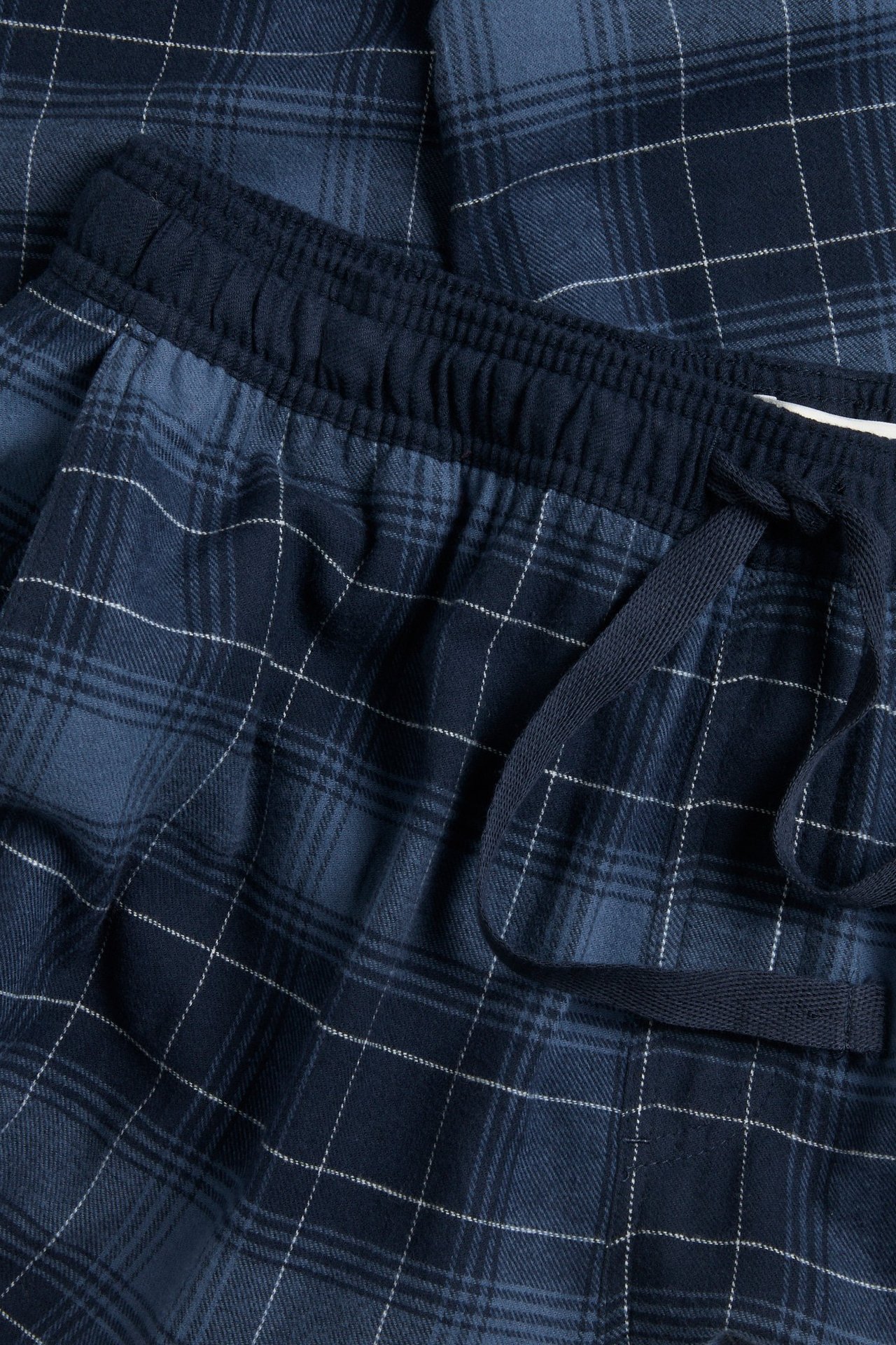 Zbliżenie męskich niebieskich piżamowych spodni w kratę z flaneli, z elastycznym pasem i sznurkiem.