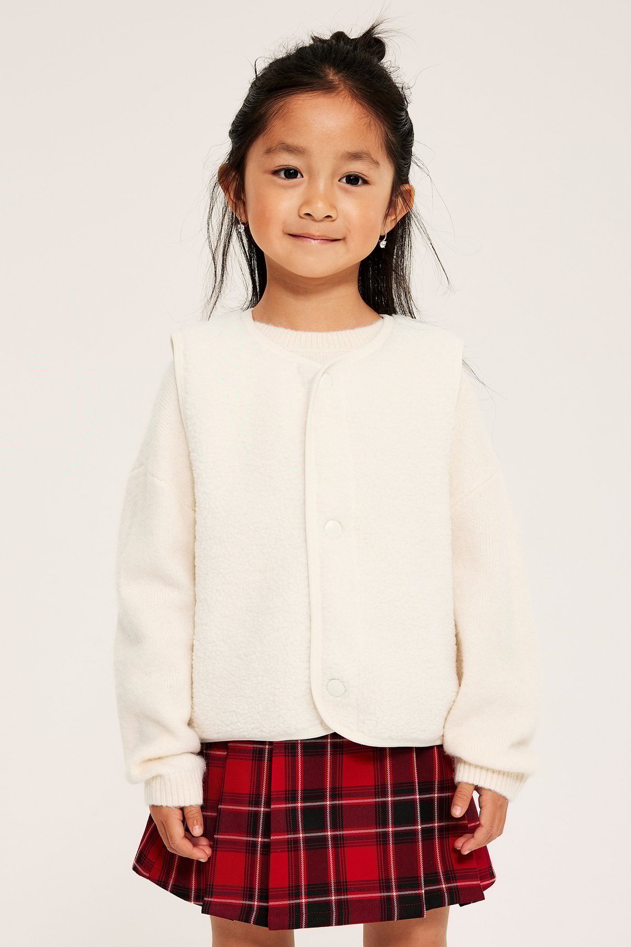 Ovanlig offwhite väst av polyester, enfärgad, bärs av flicka i röd mönstrad kjol, framvy.