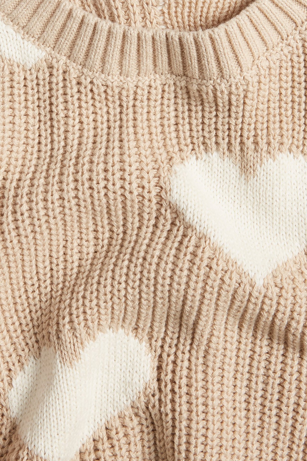 Zbliżenie beżowego, grubego swetra żakardowego z białymi sercami, wykonanego z bawełny.