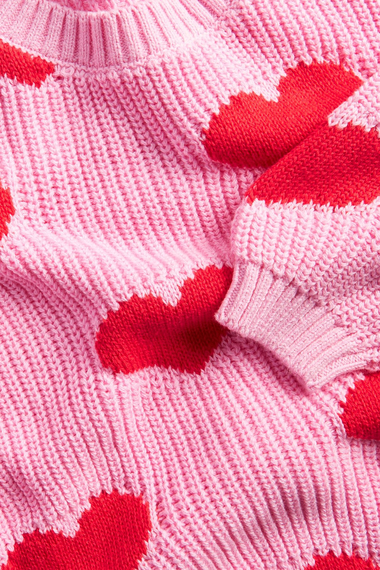 Zbliżenie na jasnoróżowy, gruby sweter bawełniany z czerwonymi sercami żakardowymi.