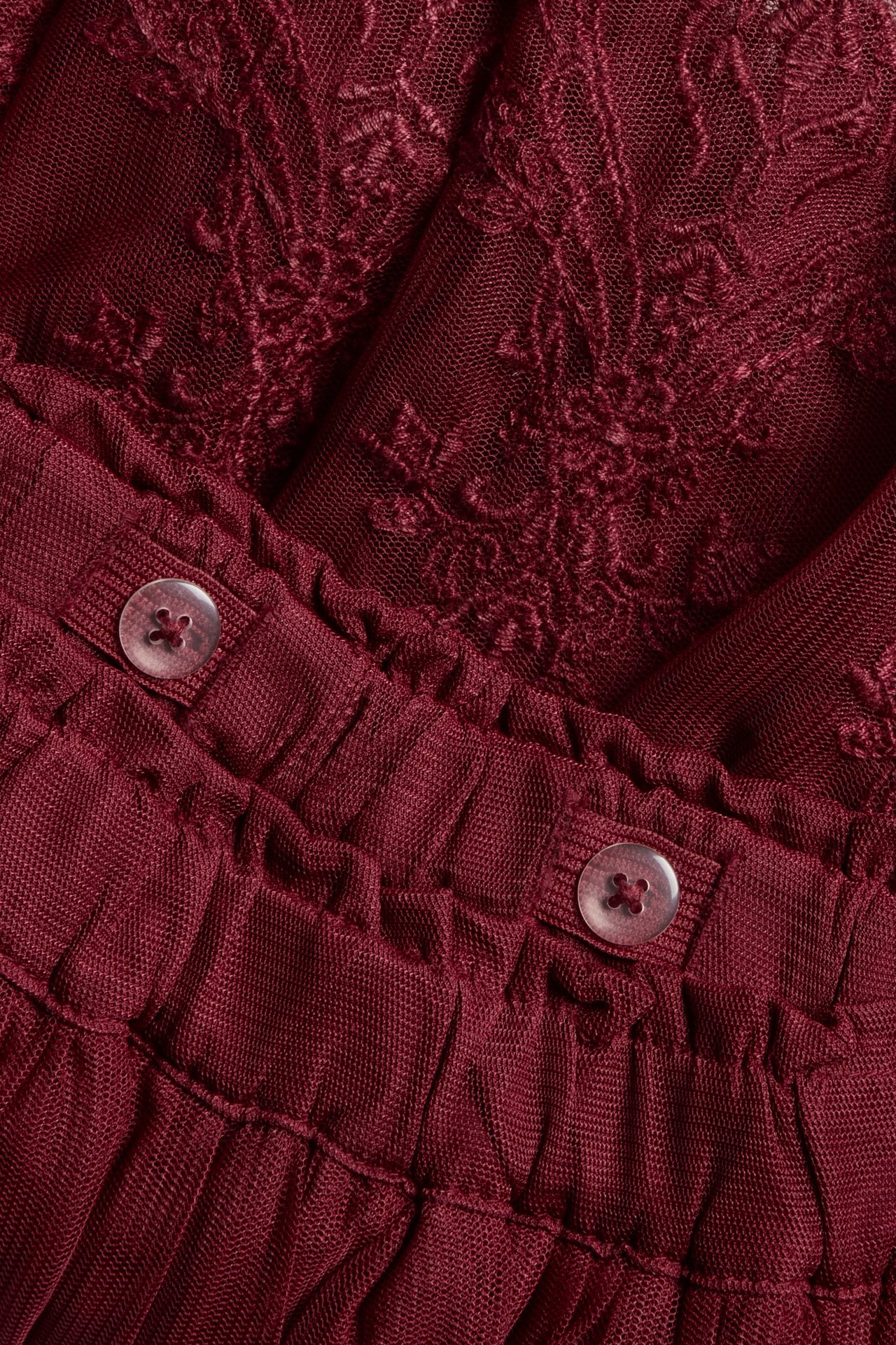 Nærbilde: rødt brodert meshskjørt for barn, justerbar elastisk linning med knapper.