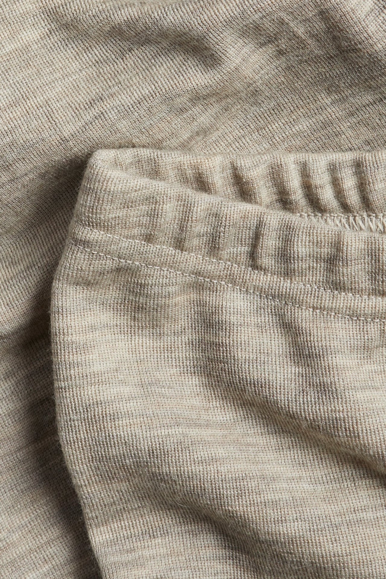 Nærbilde av et melert beige strikkeplagg med elastisk ribbet midje.