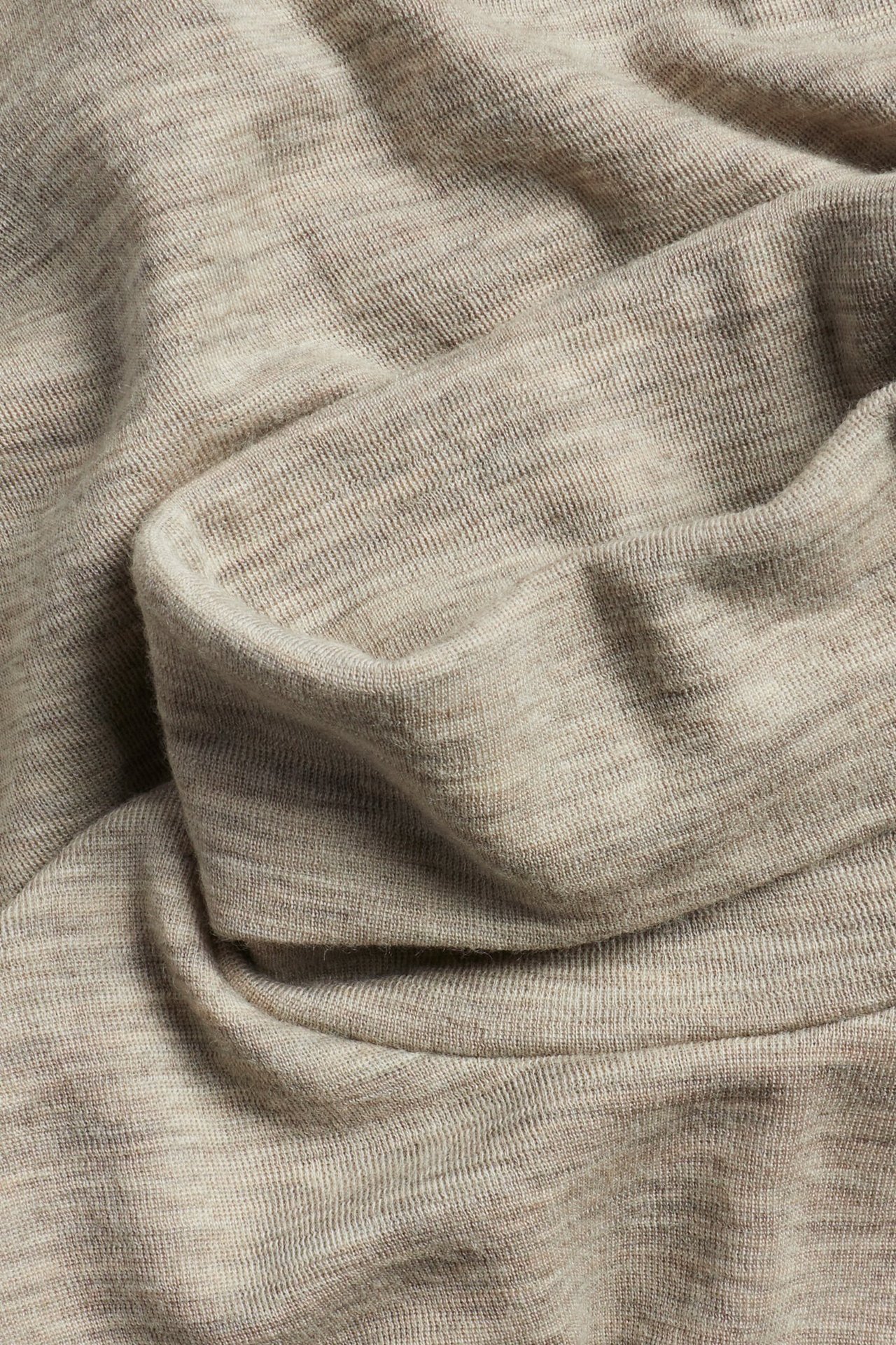 Zbliżenie beżowego melanżowego materiału swetra z golfem z wełny merynosów, miękko udrapowanego.