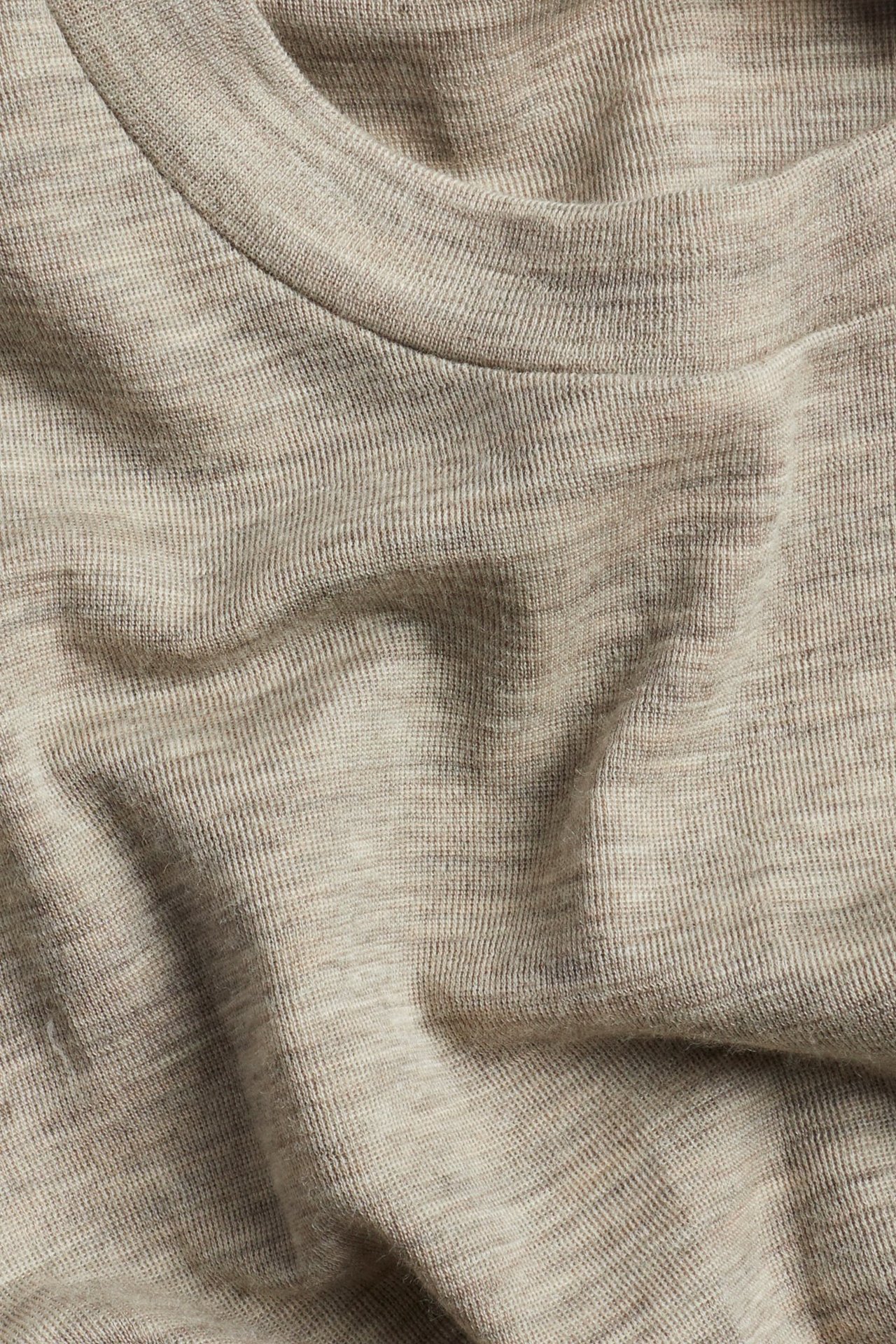 Zbliżenie beżowego melanżowego topu z wełny merynosów, ukazujące fakturę materiału i okrągły dekolt.