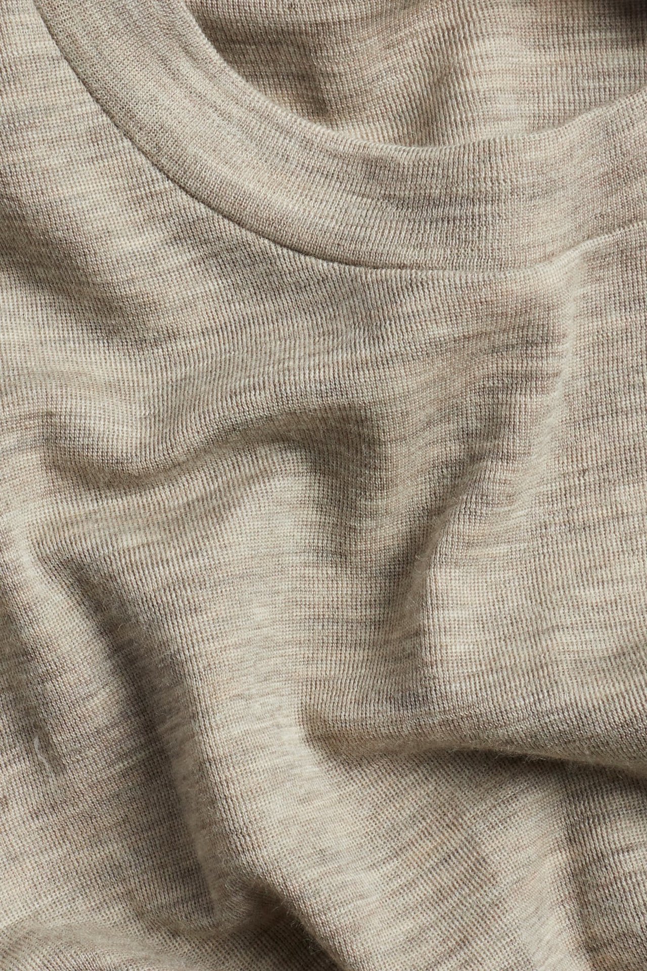 Nærbilde av en lys beige melert strikket topp med fine ribbestrikk i halsen.