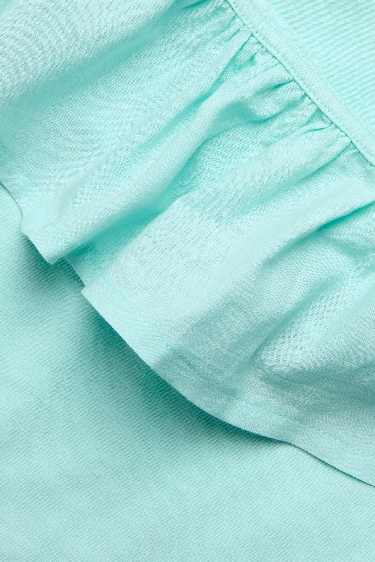 Zbliżenie na jasnoturkusowy top na jedno ramię z tkaną falbanką.