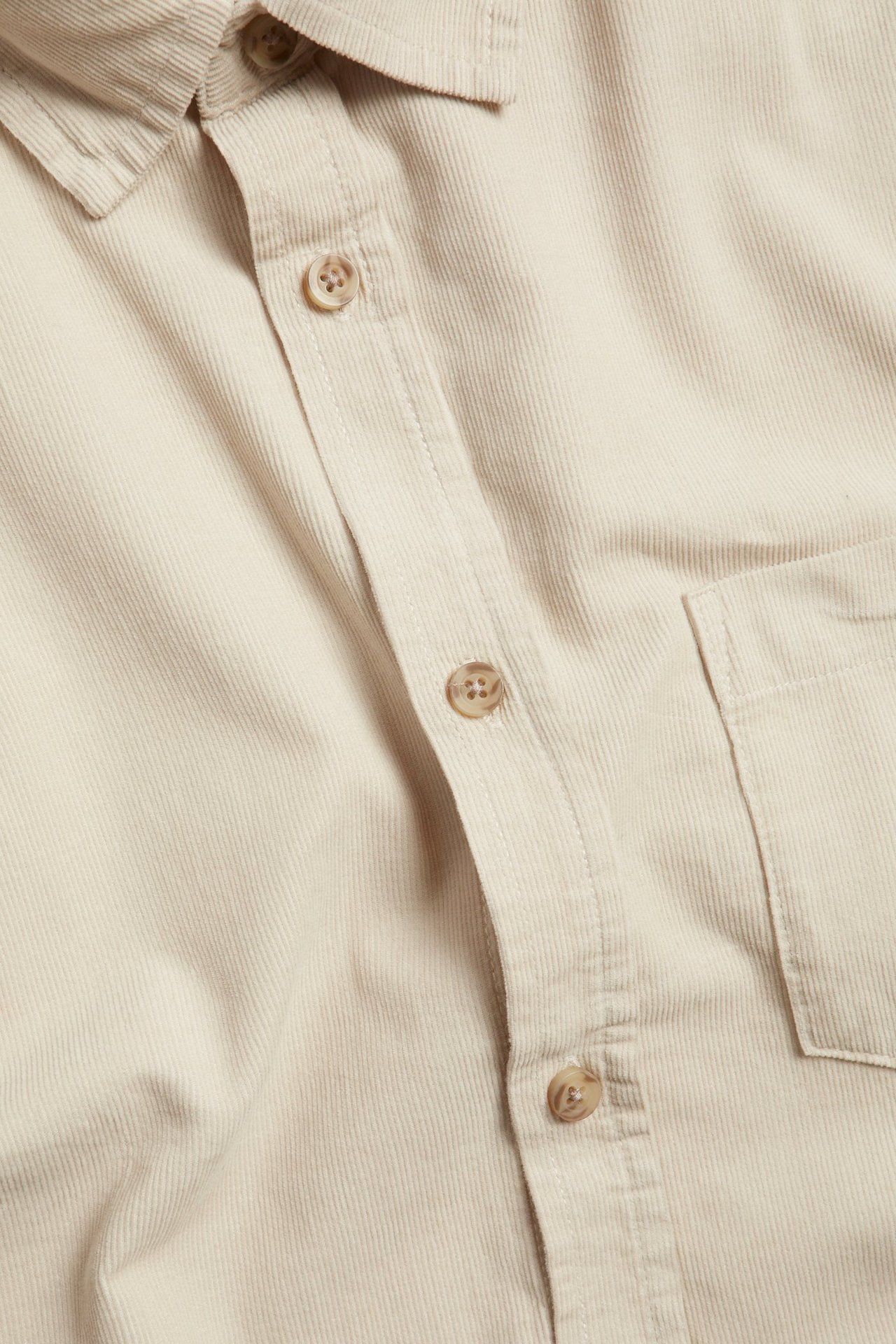Zbliżenie, widok z góry, jasnobeżowej bawełnianej koszuli sztruksowej z kołnierzem, guzikami i kieszenią.