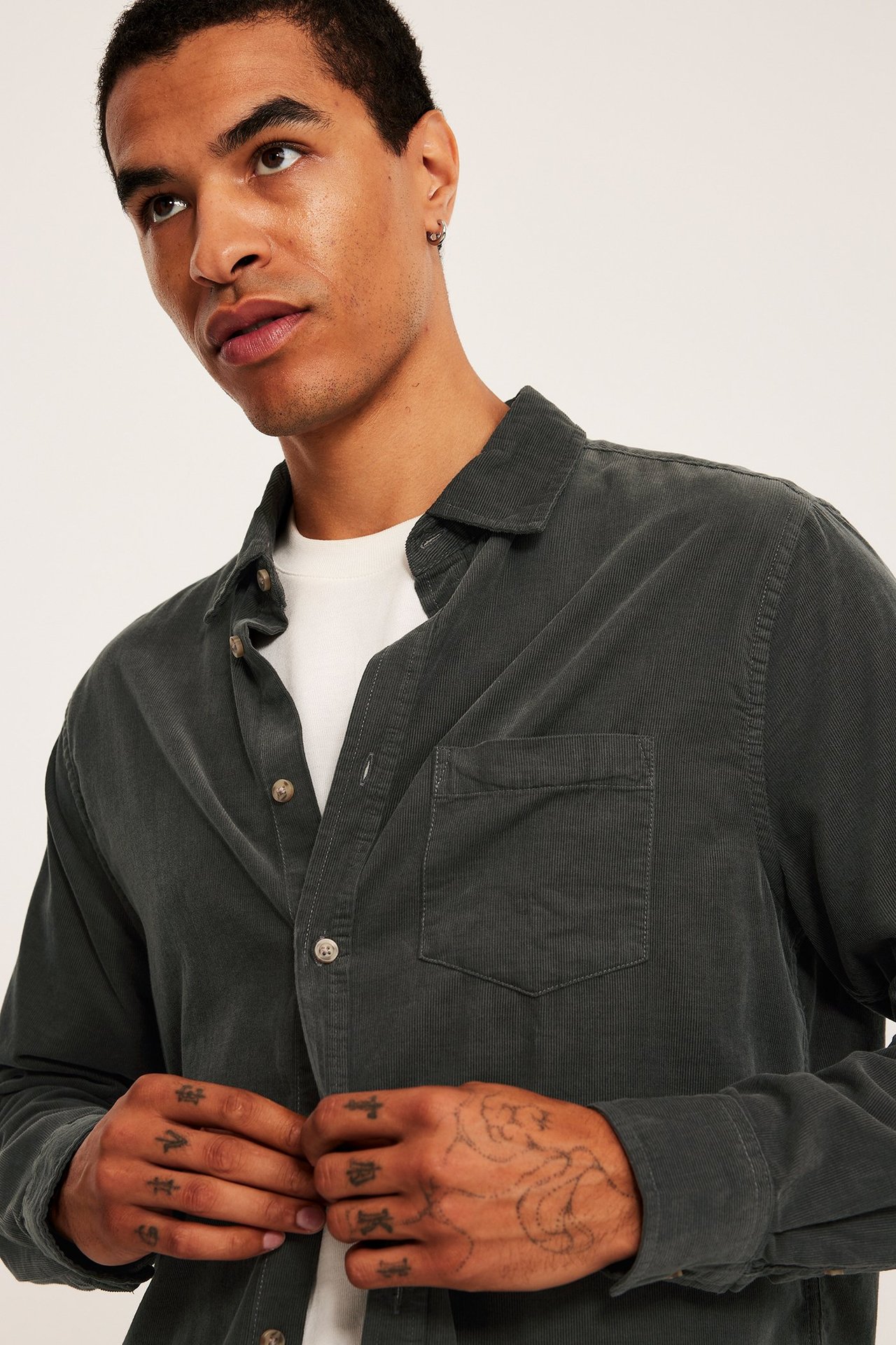 Närbild framifrån på en man i en öppen grön manchesterskjorta över en vit t-shirt.