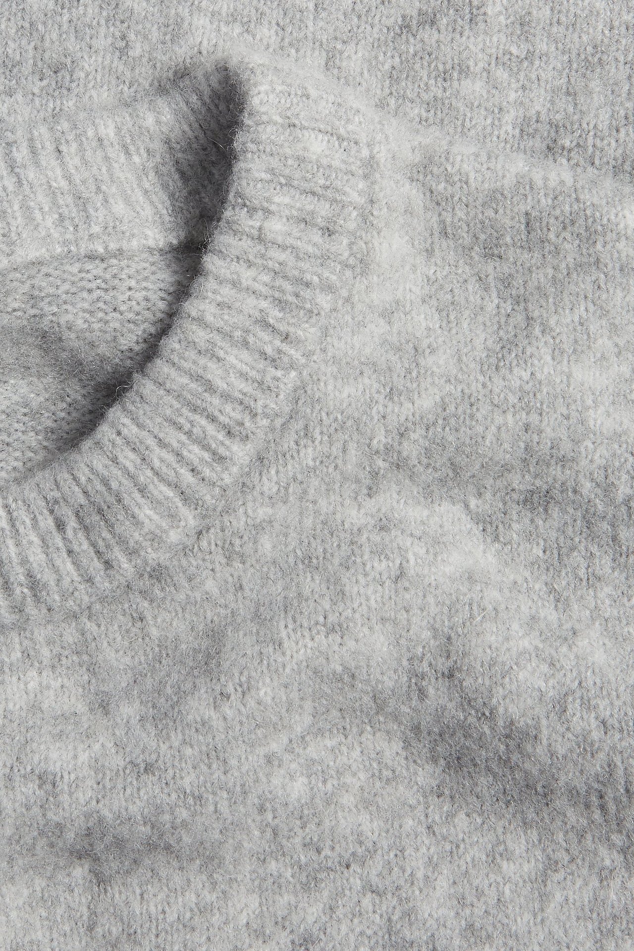 Zbliżenie na jasnoszary melanżowy, drobno dziergany sweter z krótkim rękawem i prążkowanym dekoltem.