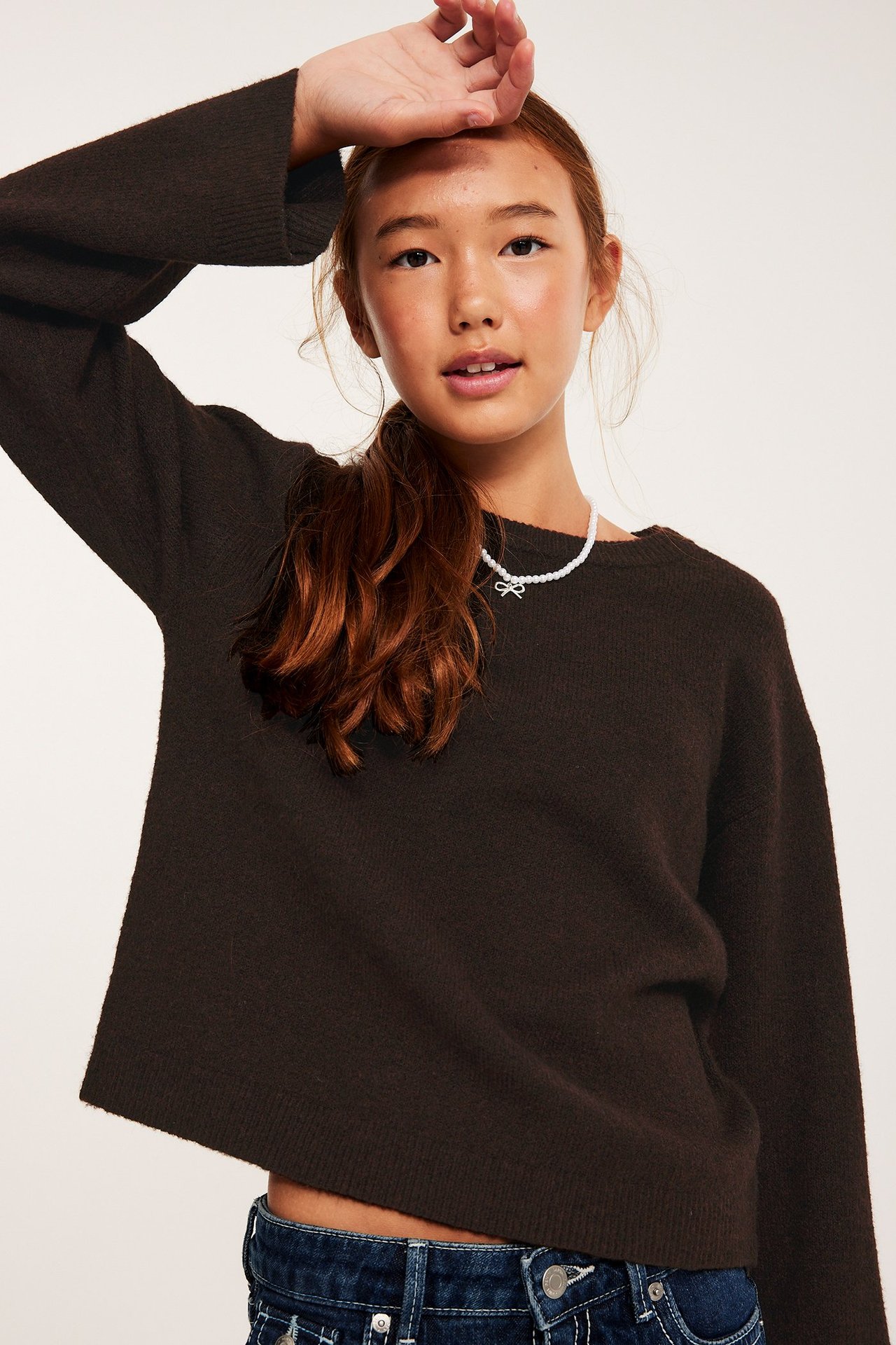 Barnkvinna i mörkbrun stickad tröja med lång ärm, frontvy.