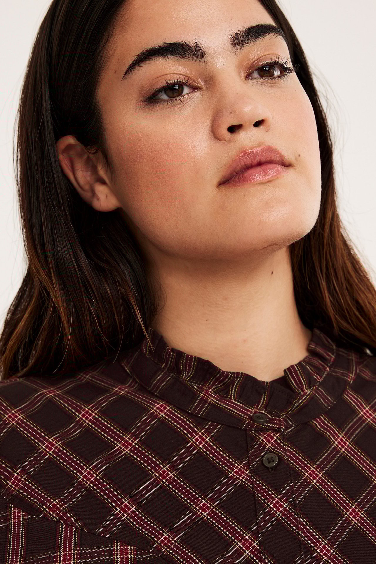 Närbild på en kvinna i vinröd rutig blus med volangkrage och knappslå.